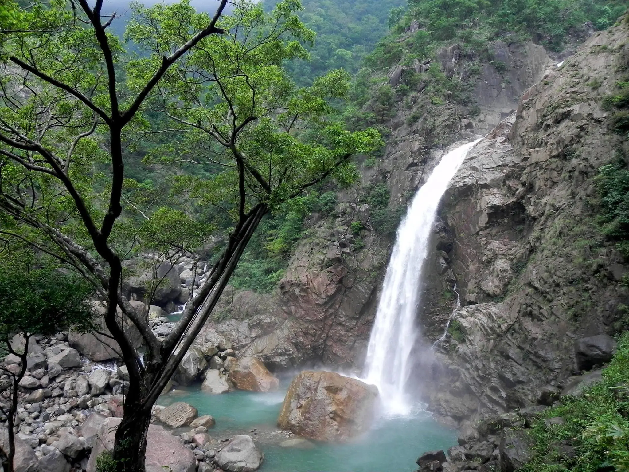 Rainbow Falls dropping down a rock face into a turquoise pool surrounded by boulders and forest