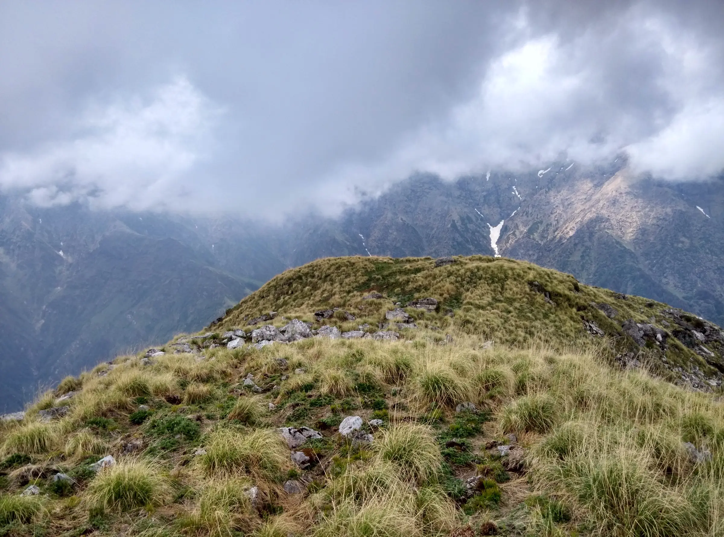 Grassy ridge at Rakhundi Top above Shilt, the optional extension of the trek, with cloud over the GHNP peaks