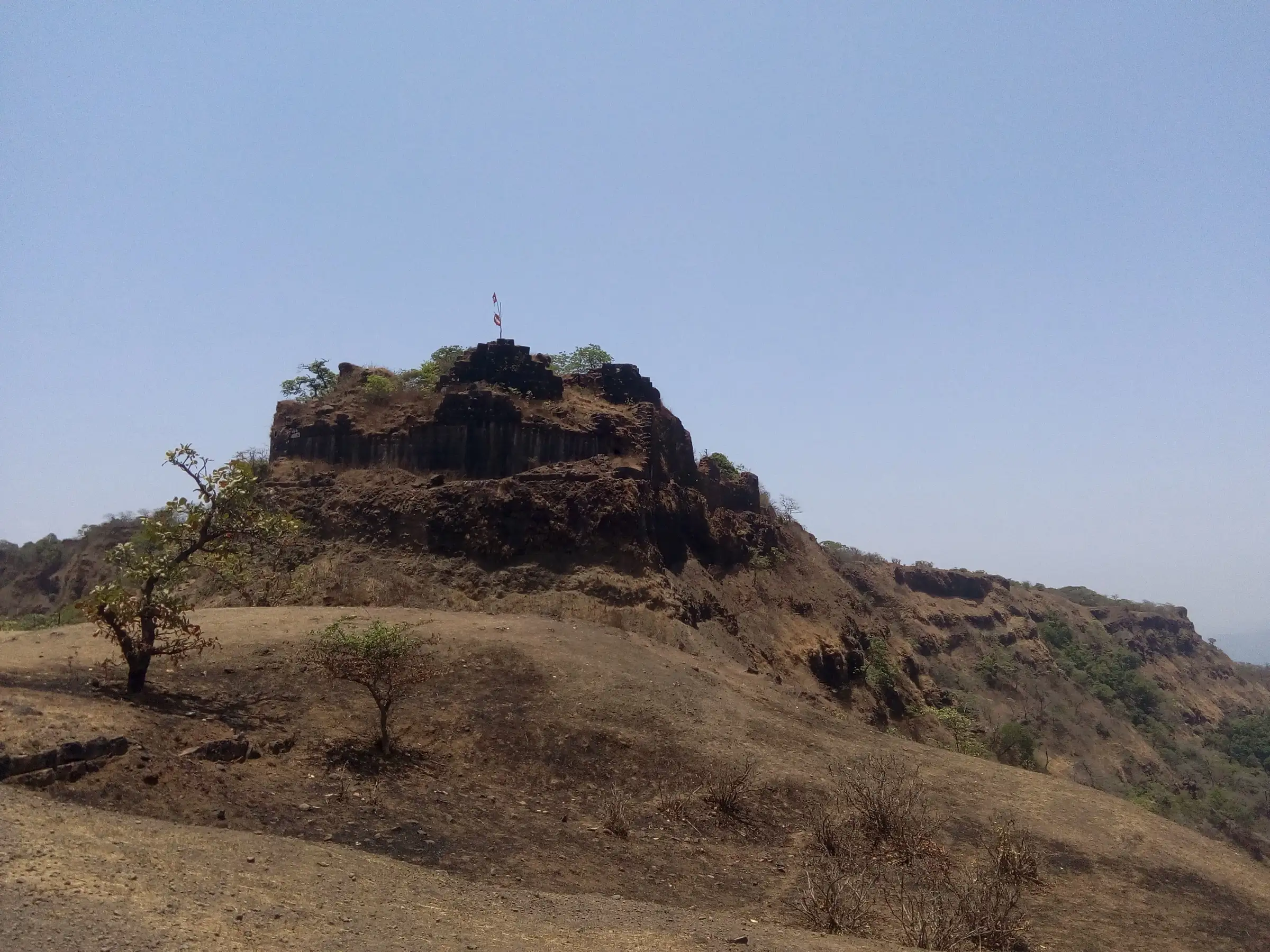 Laterite bastion of Rangana Fort with a saffron flag on top, rising above a dry grassy plateau