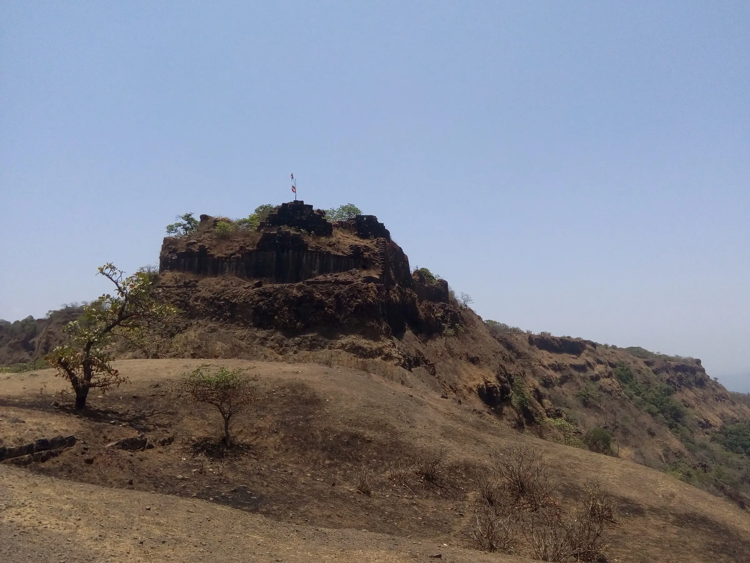 Laterite bastion of Rangana Fort with a saffron flag on top, rising above a dry grassy plateau