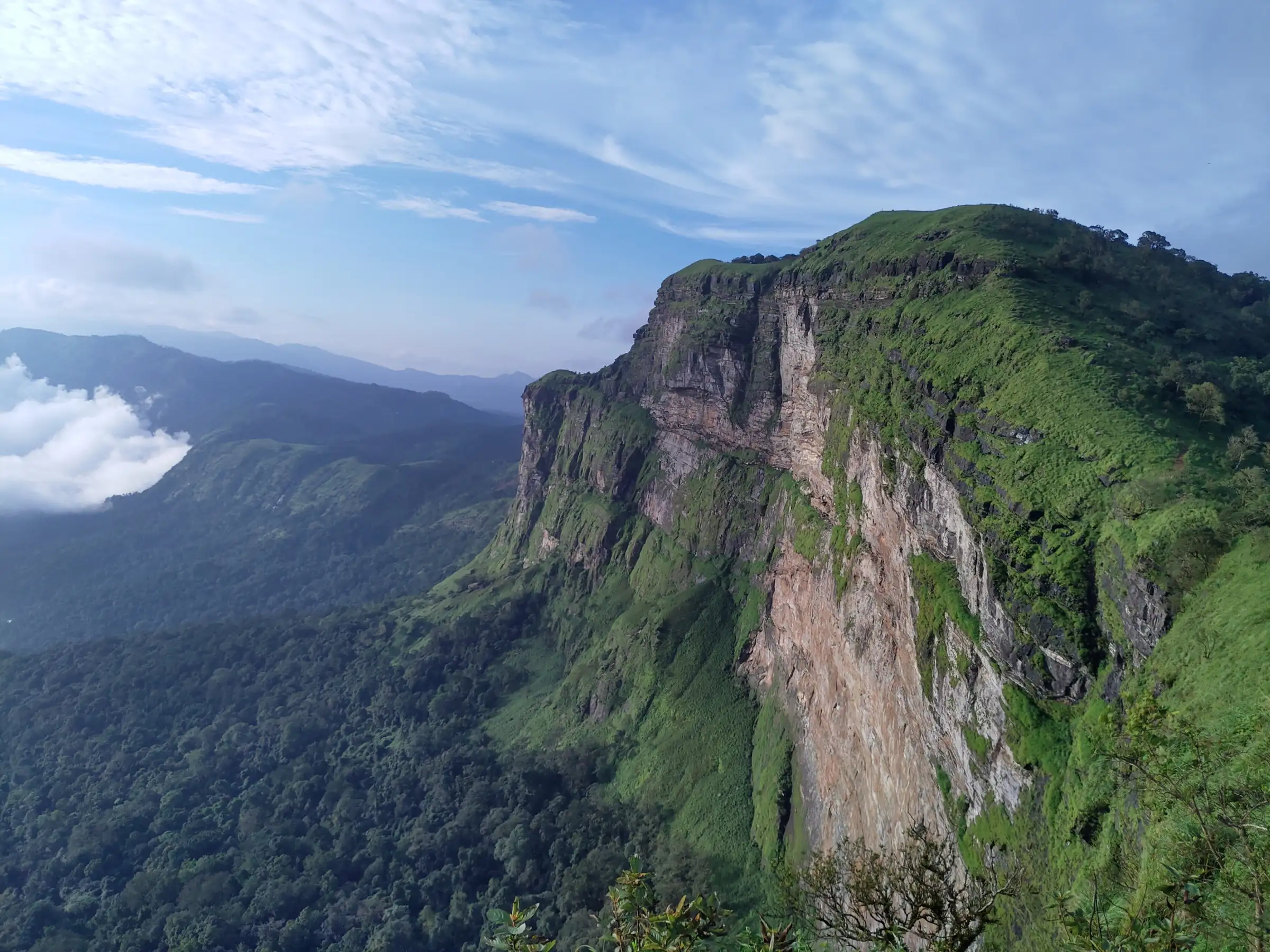 Sheer grass-topped cliff at Rani Jhari View Point near the start of the trek, above forested valleys under a blue sky