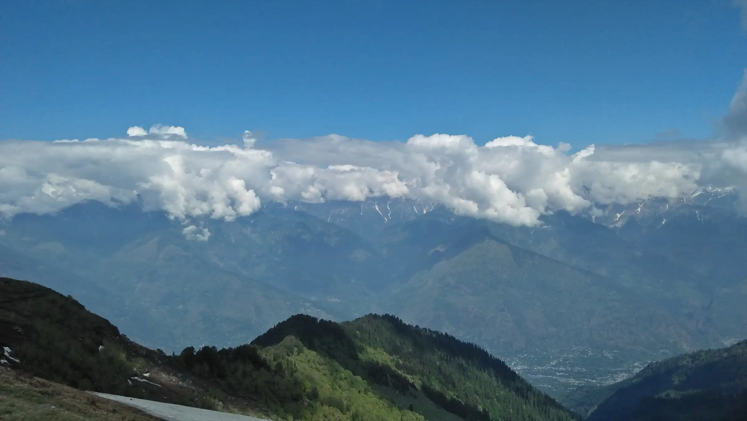 View from a high camp on the ridge near Chandrakhani Pass, close to the Dhanna Kunnu route, over forested slopes and the Kullu valley to cloud-capped snow peaks