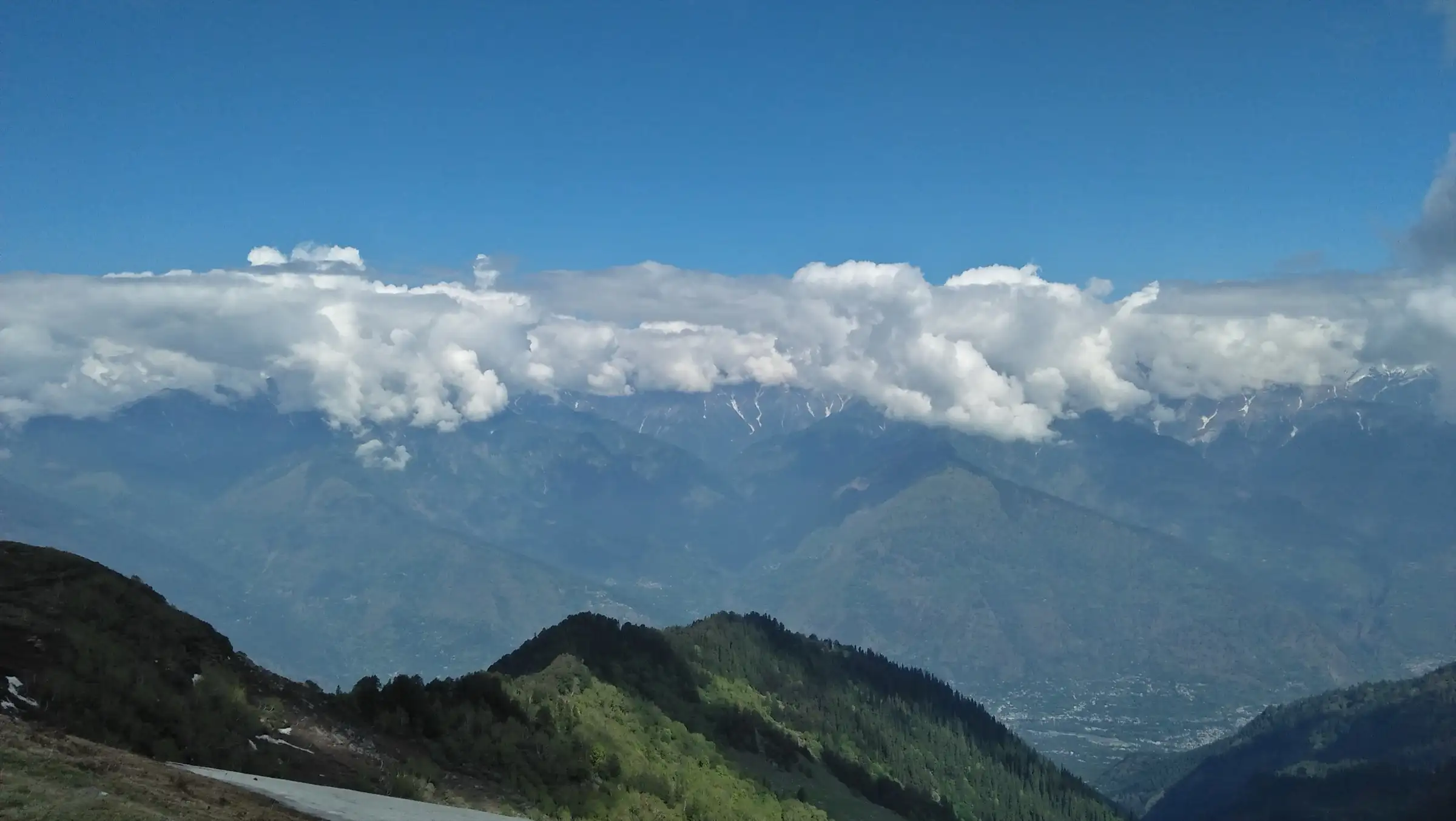 View from a high camp on the ridge near Chandrakhani Pass, close to the Dhanna Kunnu route, over forested slopes and the Kullu valley to cloud-capped snow peaks