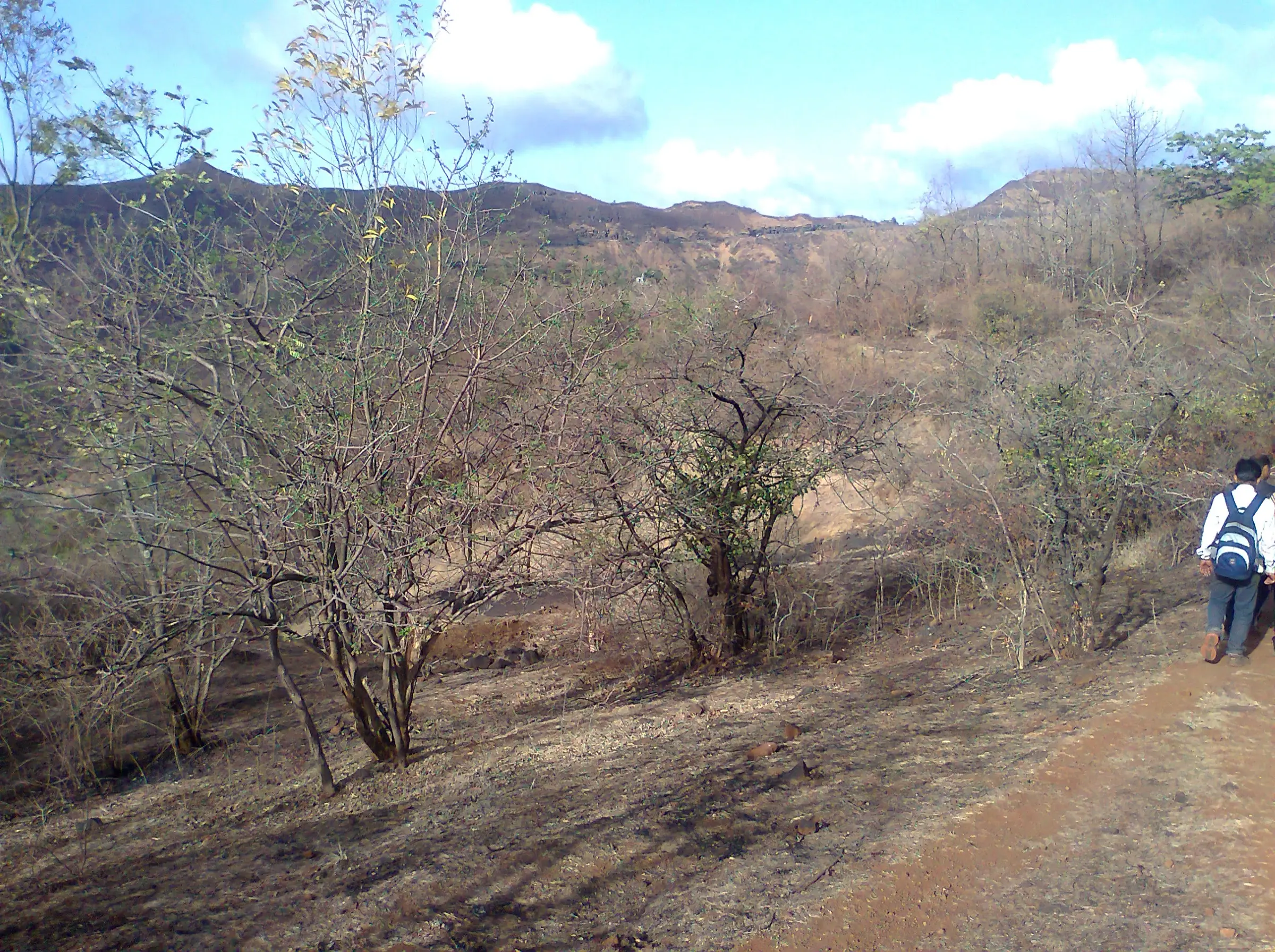 A trekker with a backpack on a dirt trail through dry scrub on the K2S ridge, with hills on the horizon