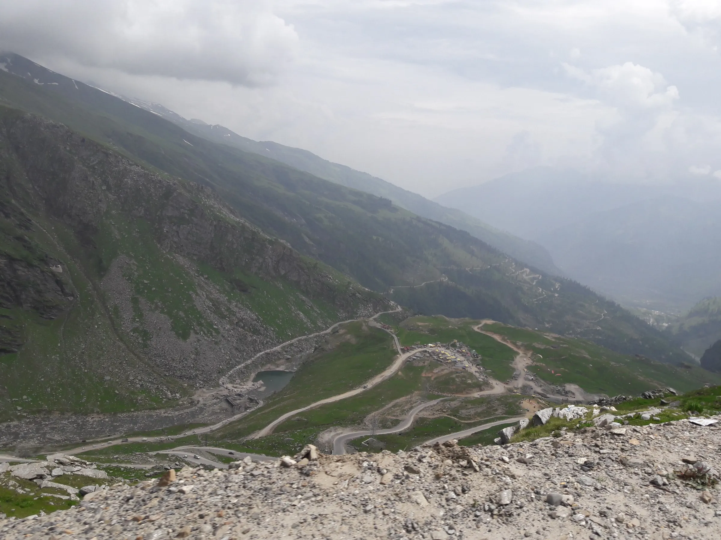 The Manali–Leh highway zig-zagging down from near Rohtang Pass towards Marhi, with green slopes and low cloud