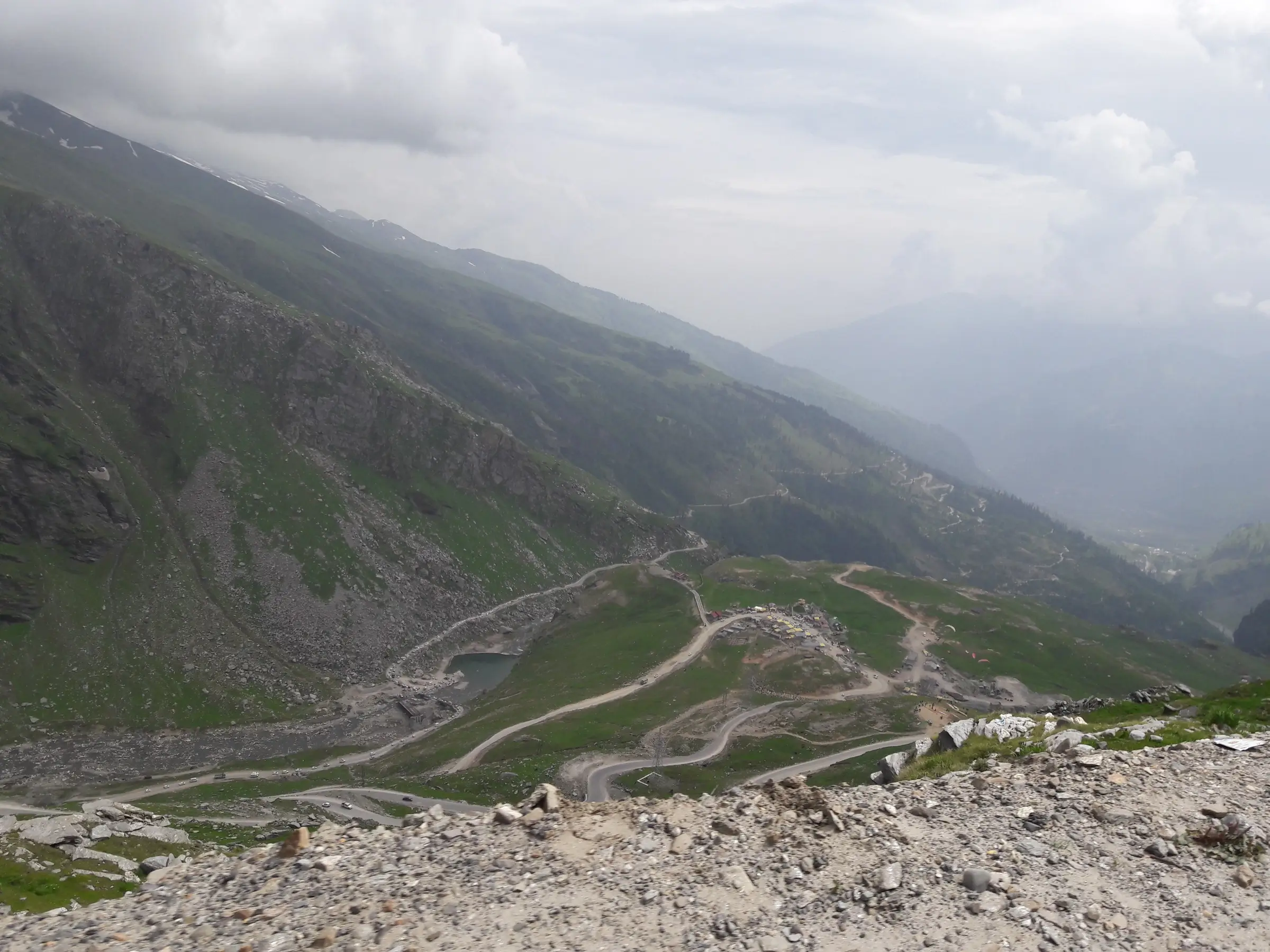 The Manali–Leh highway zig-zagging down from near Rohtang Pass towards Marhi, with green slopes and low cloud