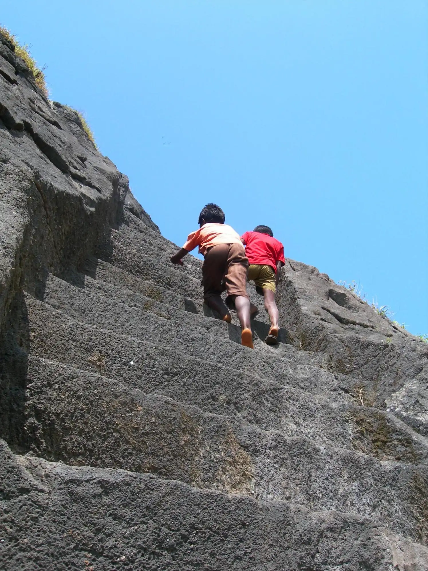 Two climbers on the steep, tall rock-cut steps leading to the summit of Kalavantin Durg