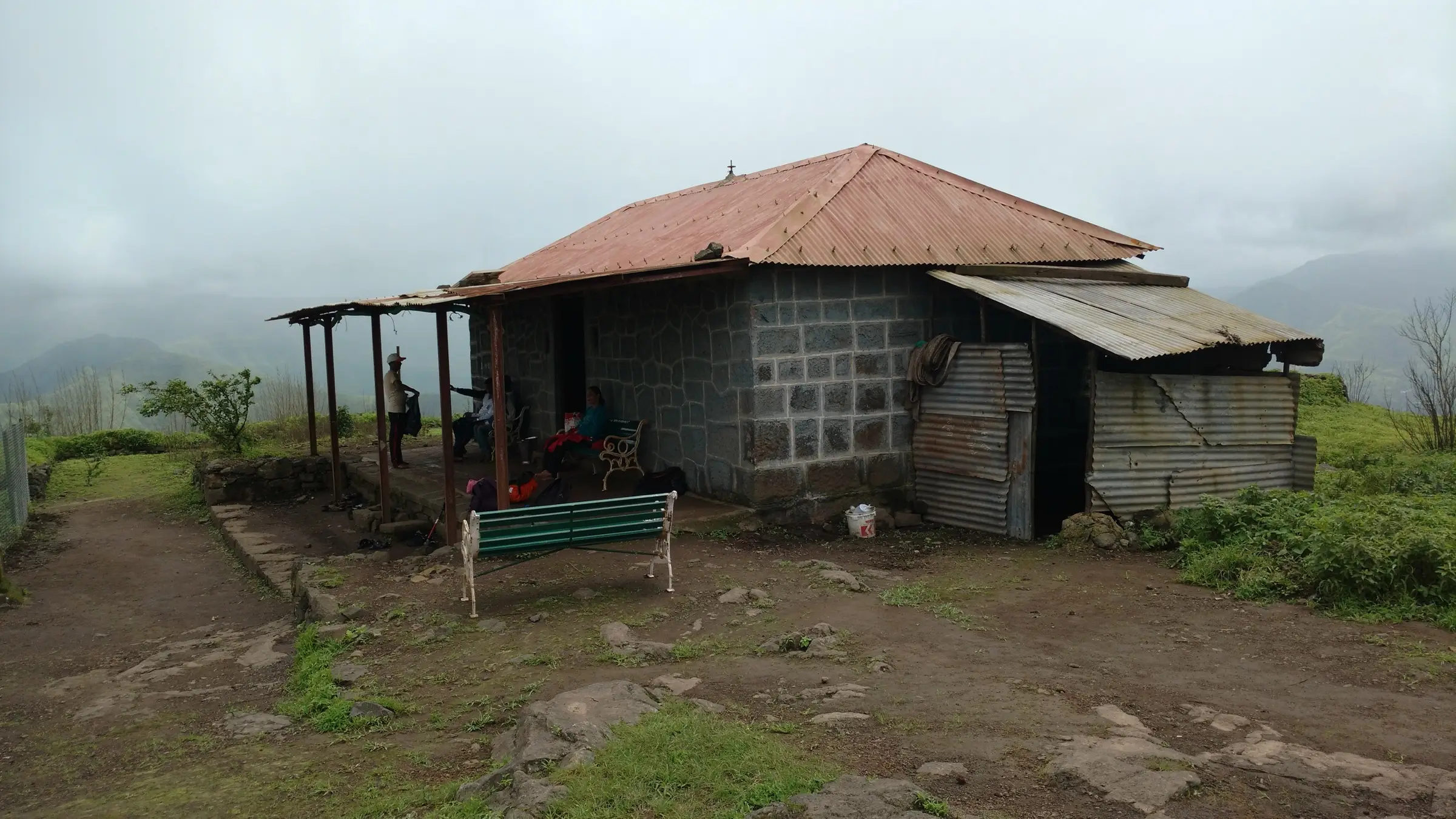 The Rohidmalla Mandir on Rohida fort, a stone-block building with a red tin roof, in monsoon mist