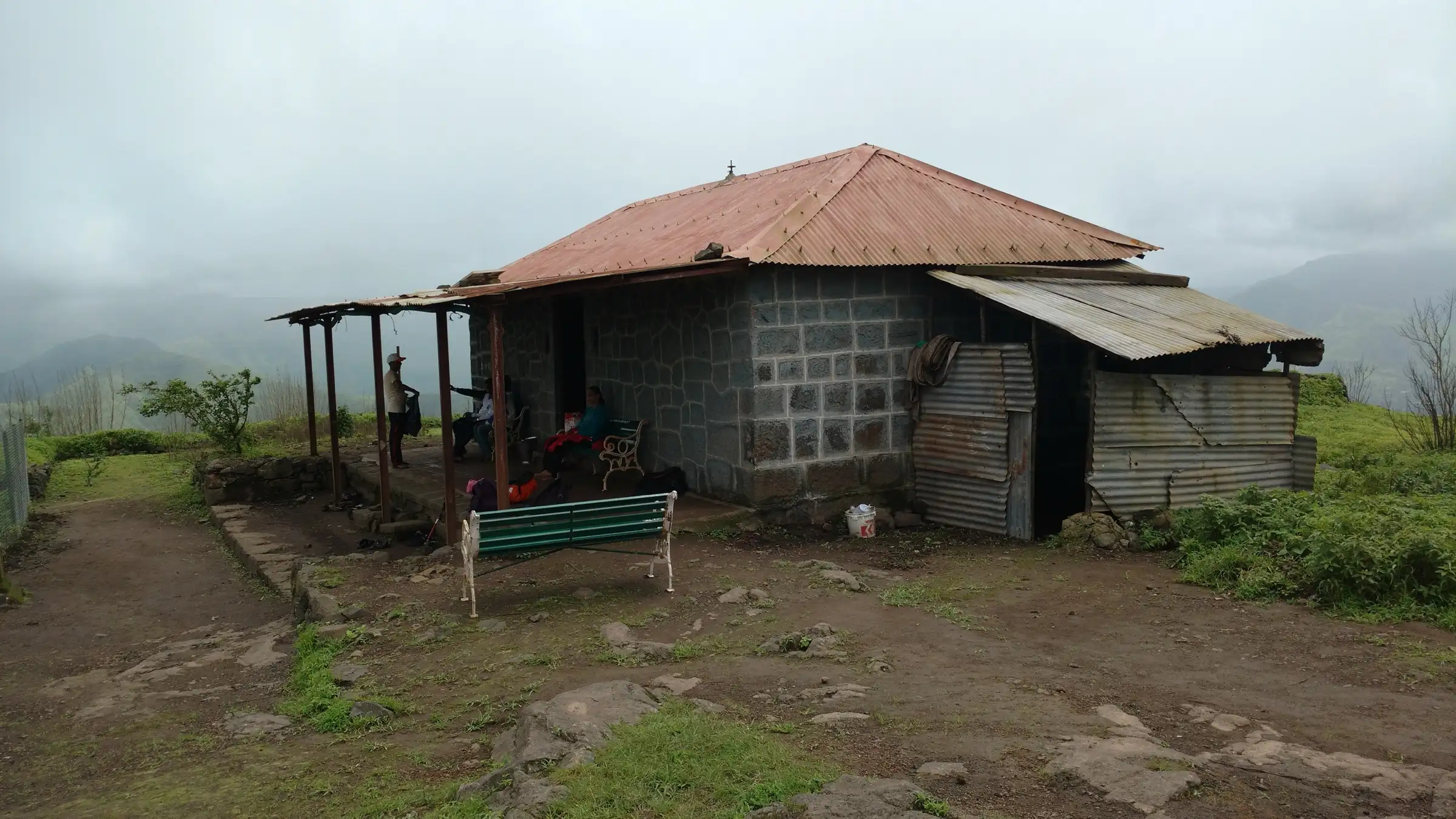 The Rohidmalla Mandir on Rohida fort, a stone-block building with a red tin roof, in monsoon mist