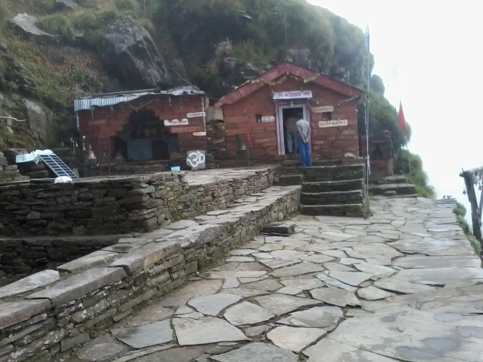Small stone and brick shrines of Rudranath built into a mountain rock face, reached by a flagstone path in the mist
