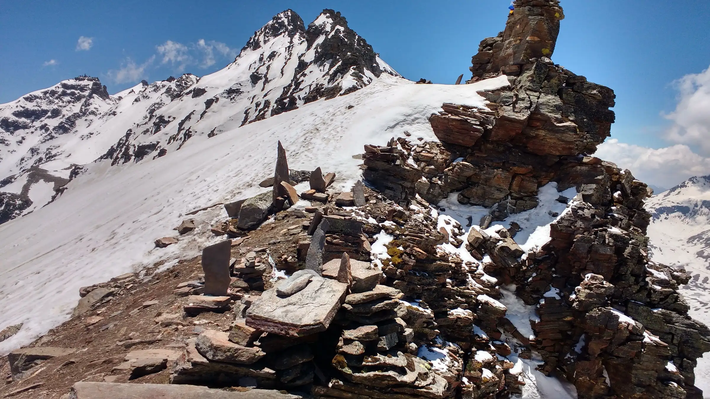 Stone cairns and stacked rock slabs on the snowy ridge of Rupin Pass with rocky peaks behind