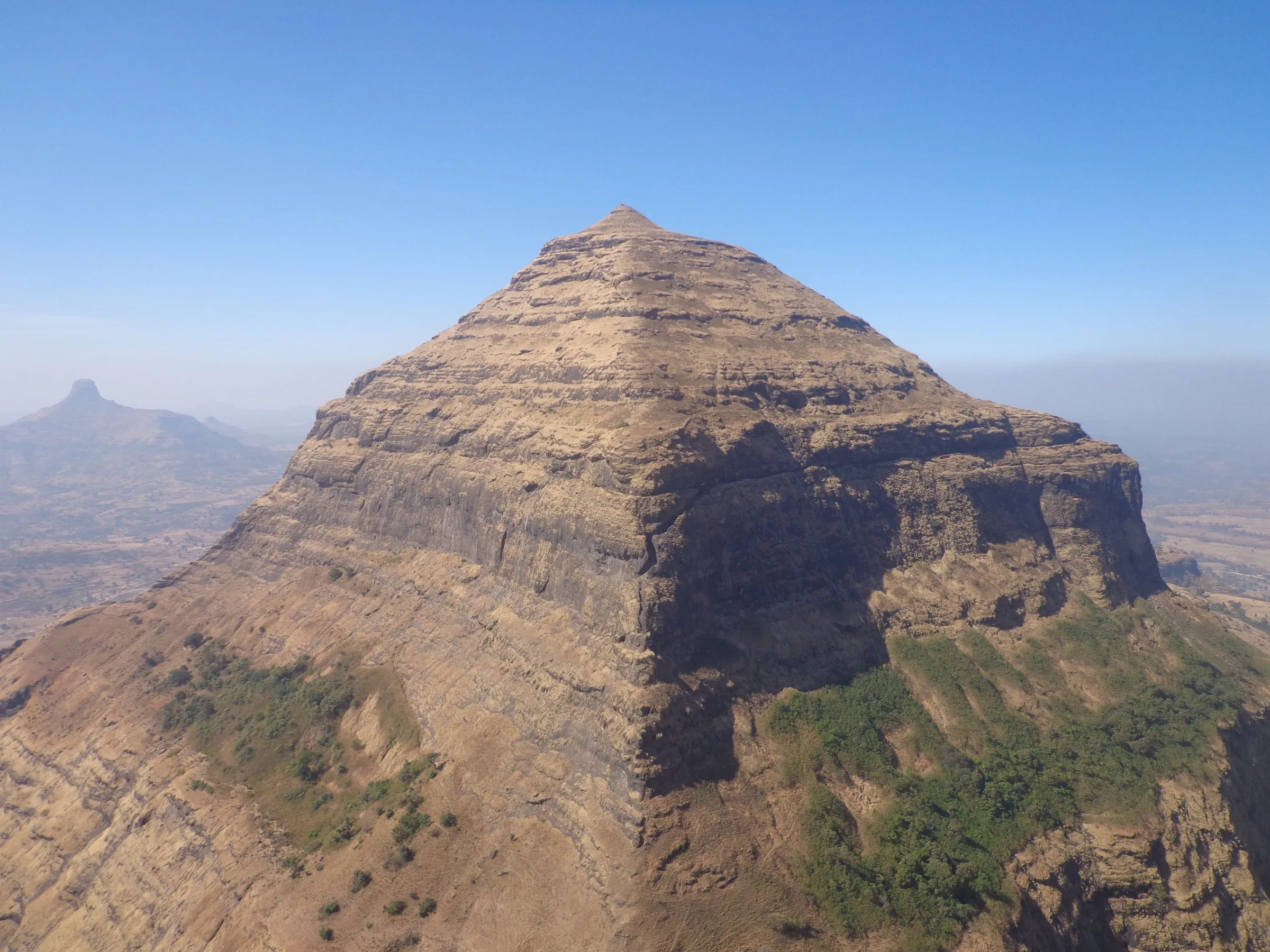 The pyramid-shaped Salher hill with sheer rock bands under a clear blue sky, a lone pinnacle on the hazy horizon