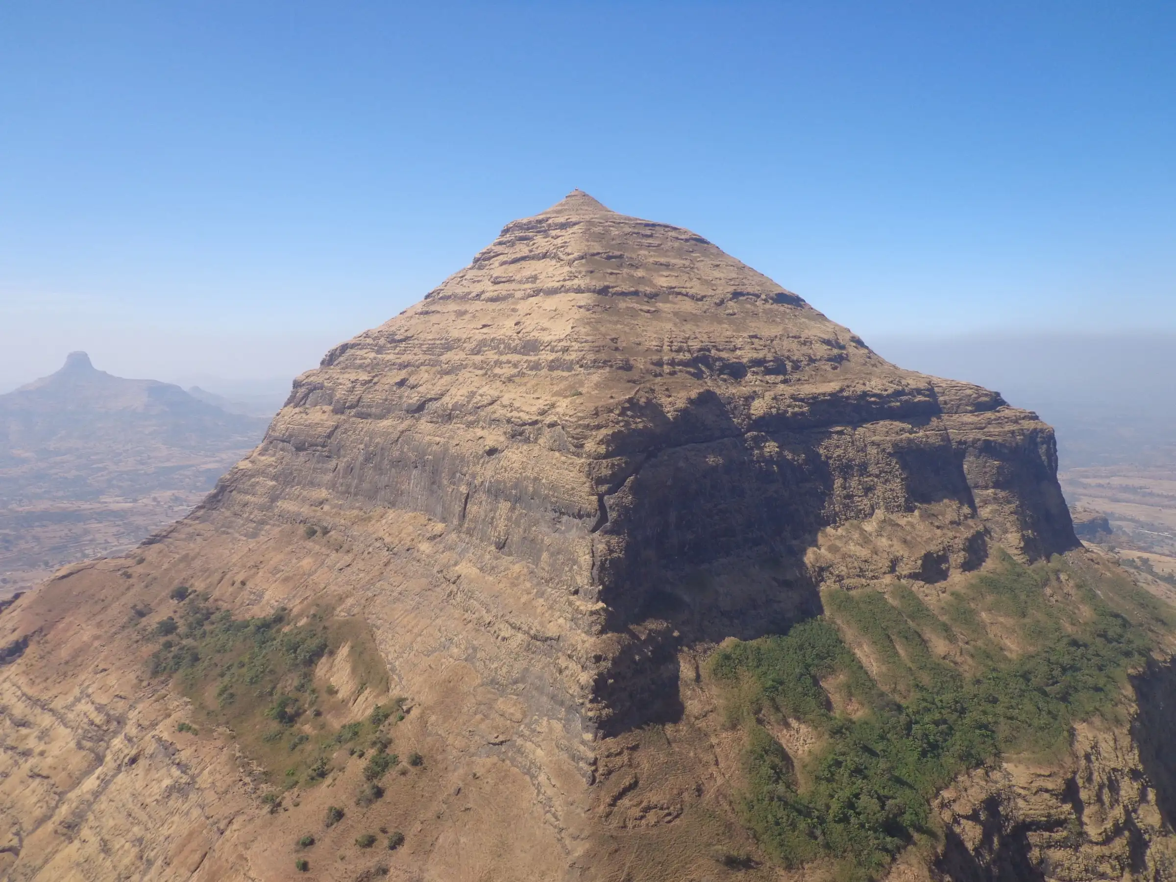 The pyramid-shaped Salher hill with sheer rock bands under a clear blue sky, a lone pinnacle on the hazy horizon