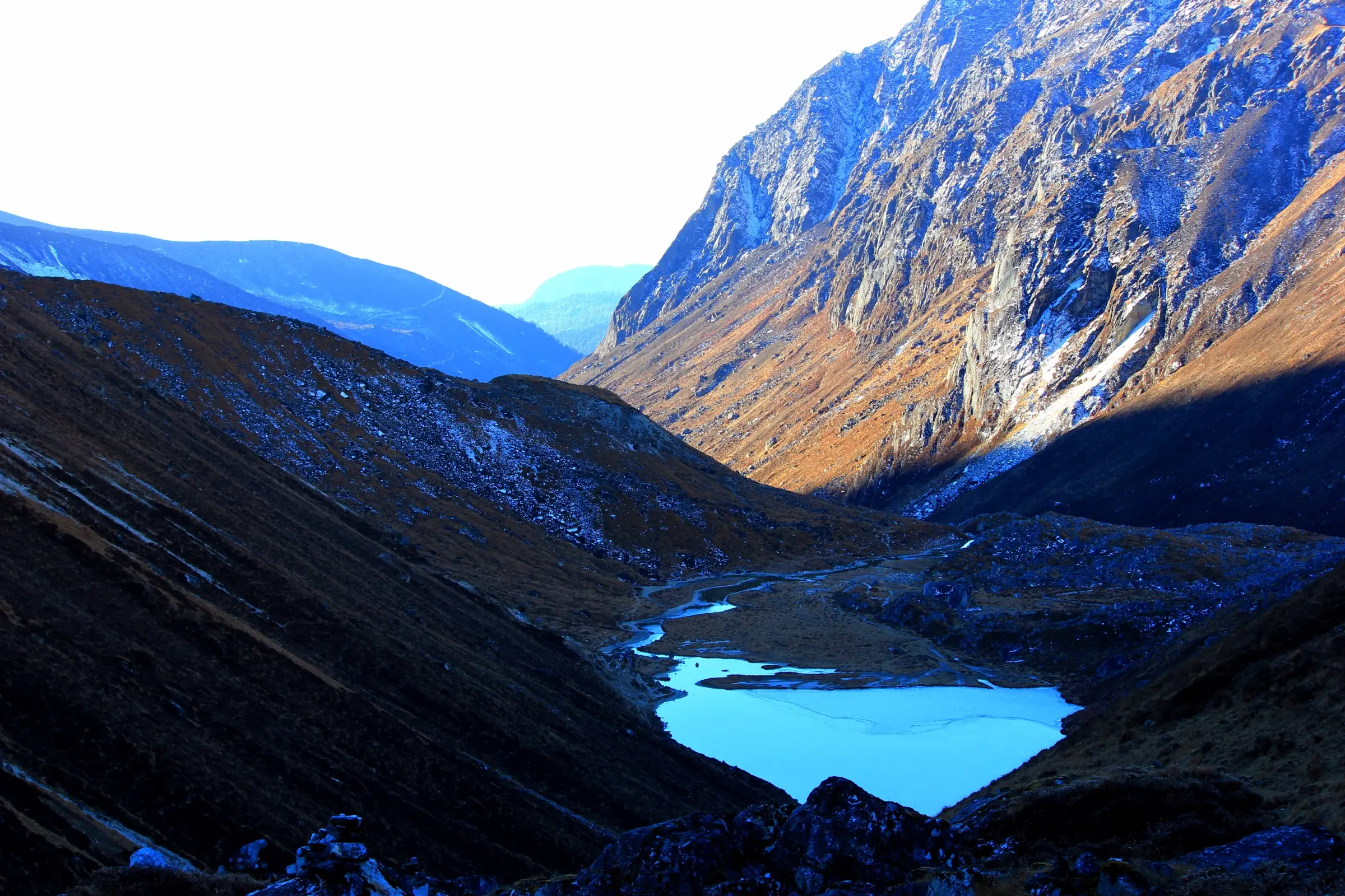 Partly frozen Samiti Lake in a bare brown glacial valley with steep rock walls catching morning light