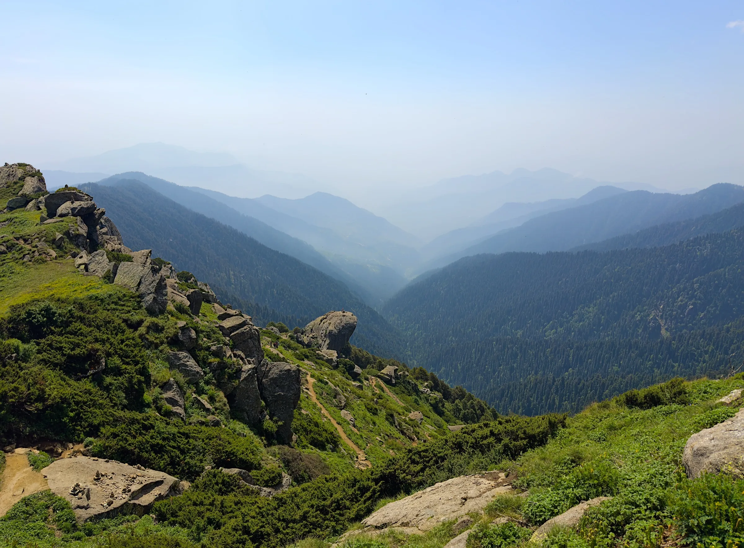 Rocky grass slopes near the top of Churdhar looking down over forested ridges of the Churdhar Wildlife Sanctuary towards the Tons valley