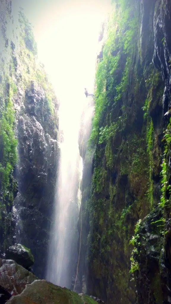 A trekker rappelling beside a waterfall between mossy rock walls inside Sandhan Valley