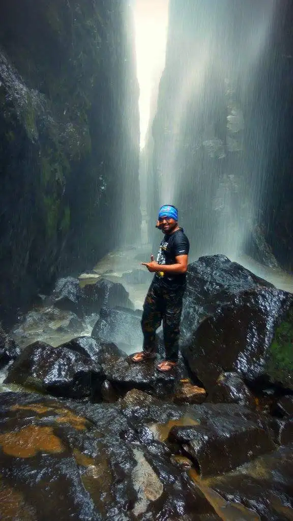 A trekker on wet boulders under a monsoon waterfall inside Sandhan Valley, upstream of the Karoli valley (nearby area, not the Karoli trail itself)