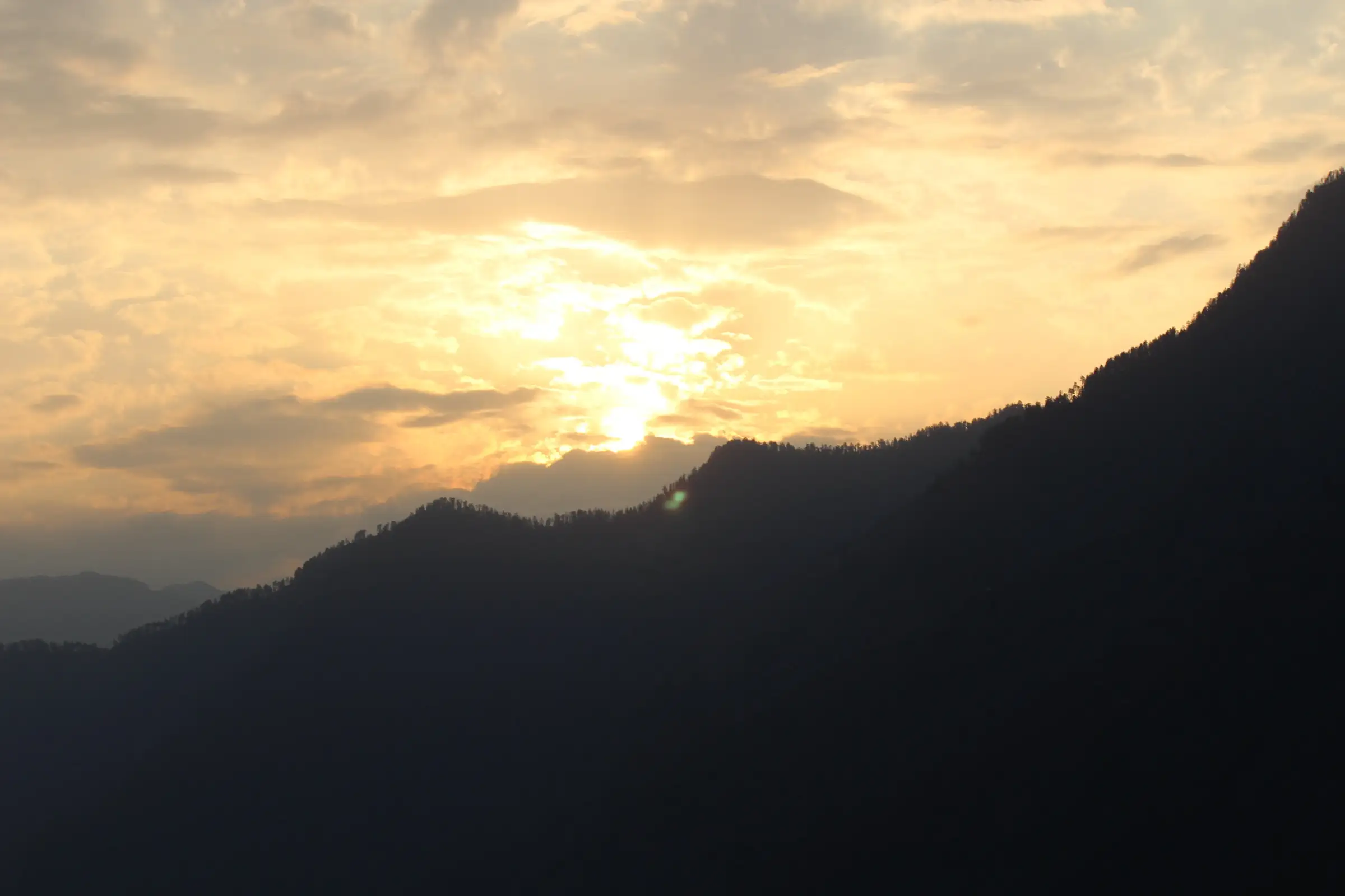 The sun setting through cloud behind a forested ridge at Sankri, the base village for this trek