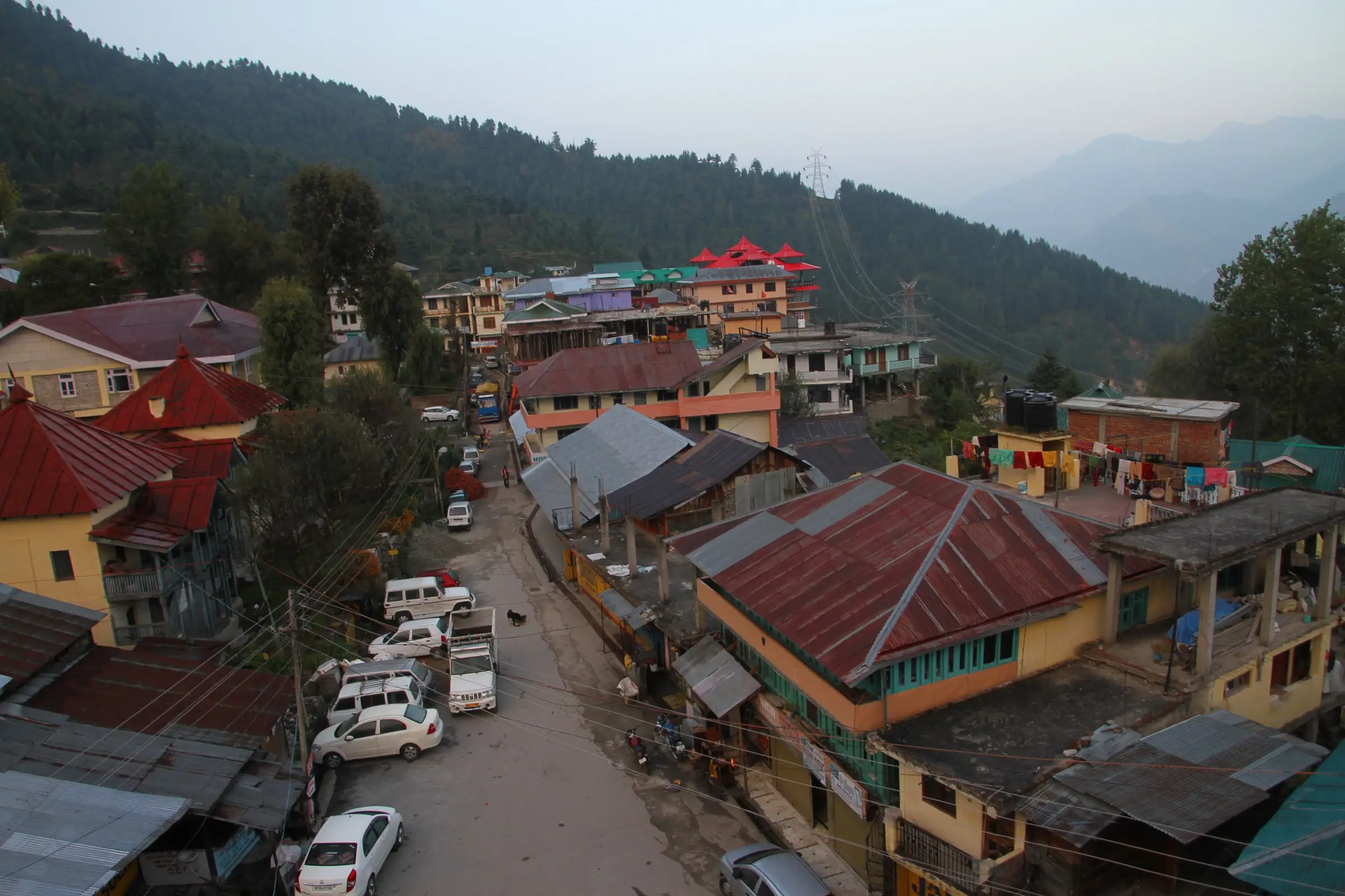 Red and green tin roofs of Sarahan village below forested slopes at dusk, the base village for the trek
