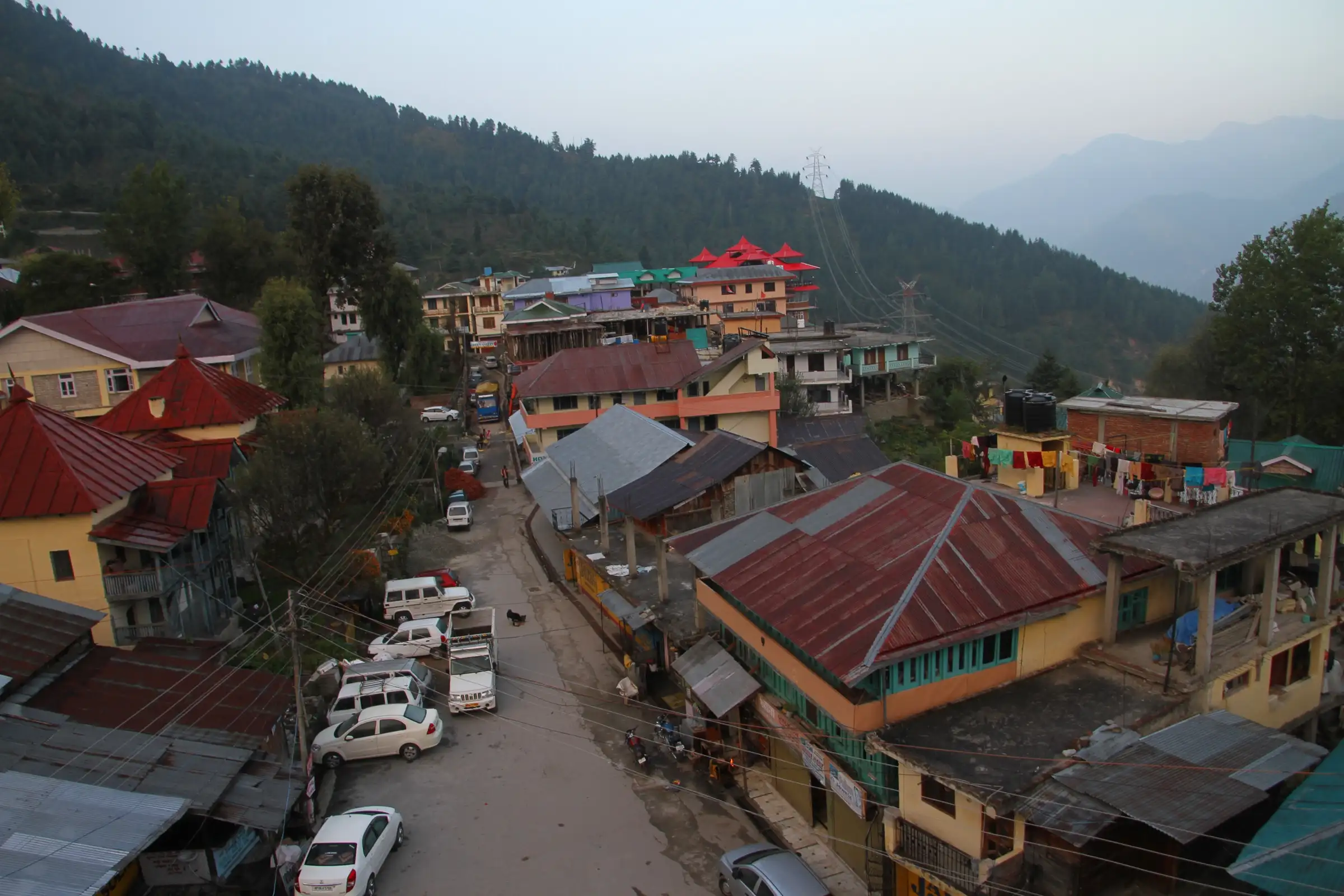 Red and green tin roofs of Sarahan village below forested slopes at dusk, the base village for the trek