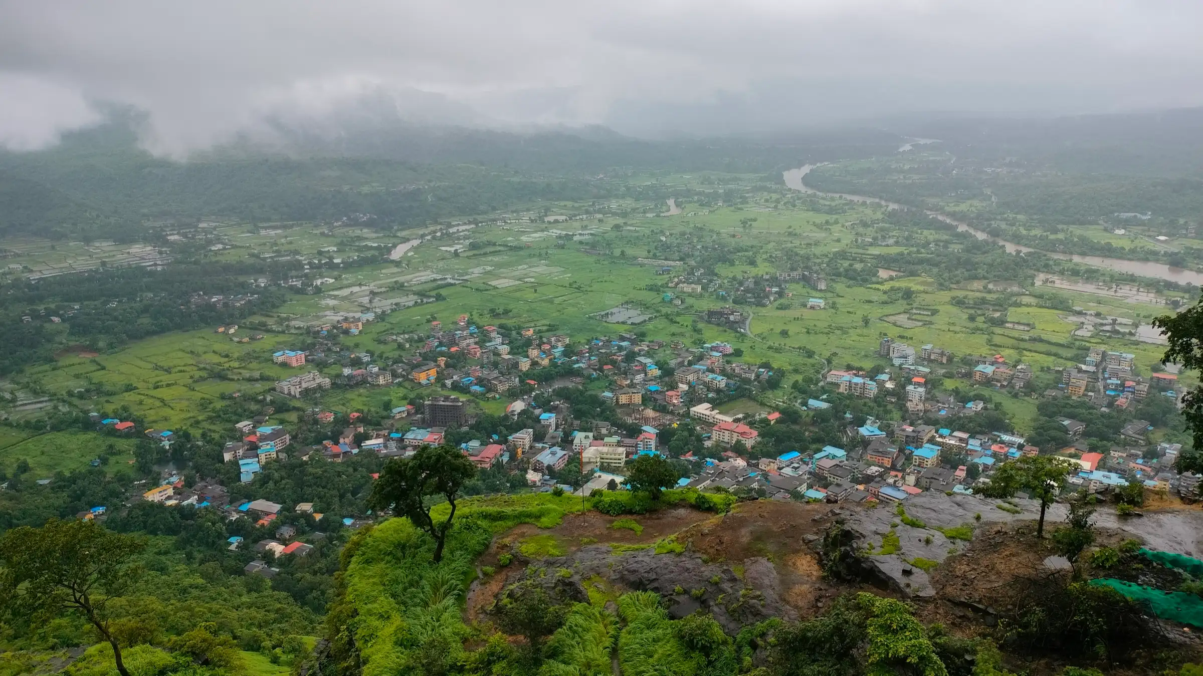 Pali town and green monsoon fields seen from the edge of Sarasgad fort under low cloud