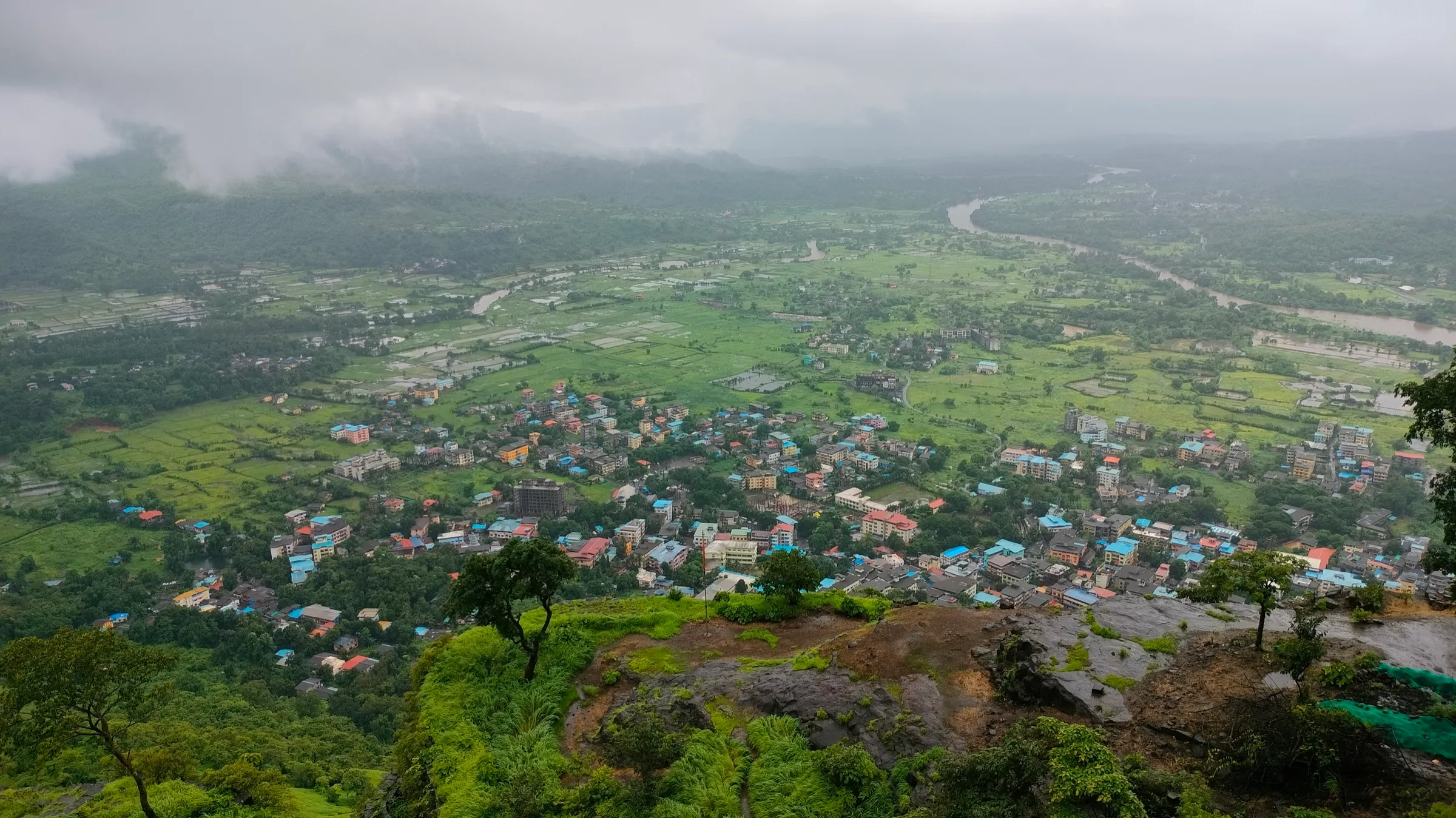 Pali town and green monsoon fields seen from the edge of Sarasgad fort under low cloud