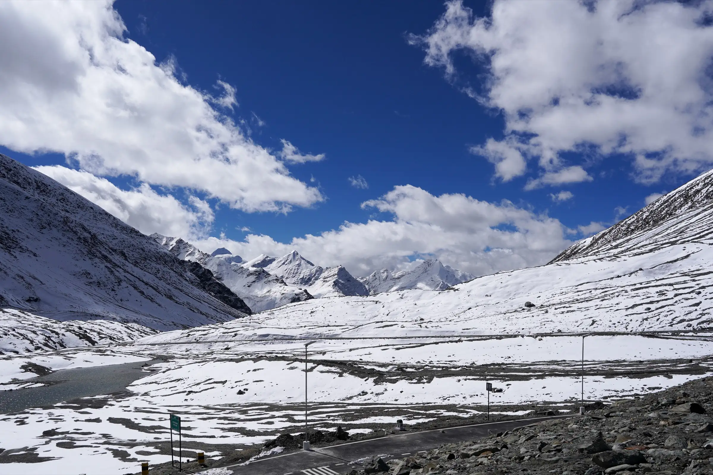 Small lake at the top of Shingo La with the new road to Darcha winding beyond it and snow peaks on the horizon