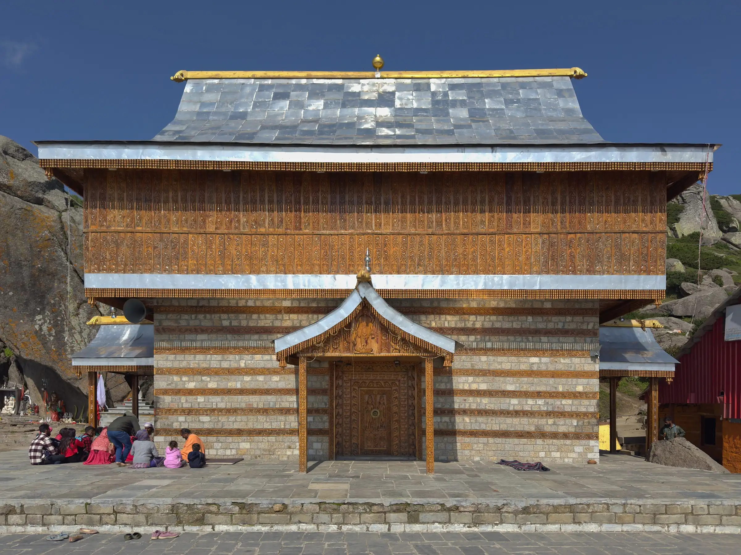 The wood-and-stone temple of Shri Shirgul Maharaj at Churdhar with devotees sitting on the courtyard
