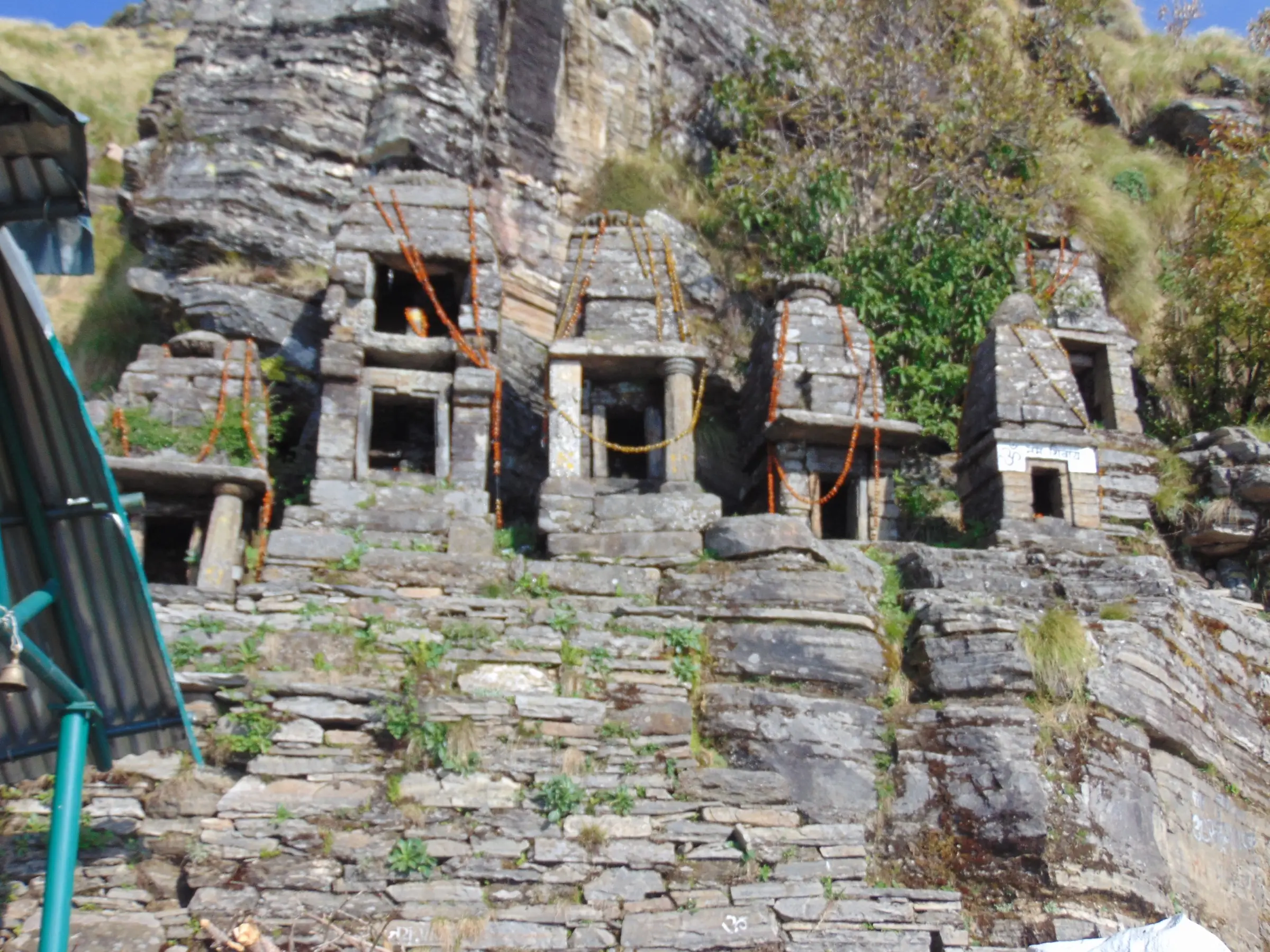 Row of small stone shrines built into the rock face beside Rudranath temple, tied with sacred threads