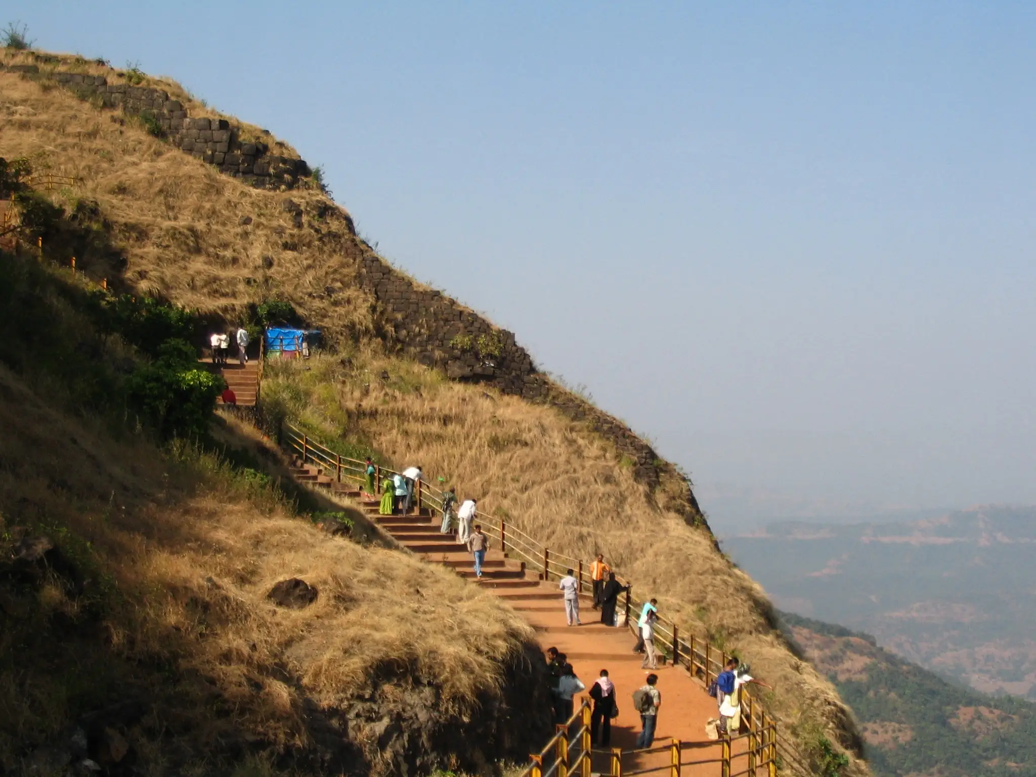 Visitors climbing the railed stone stairway up the grassy slope to Vishalgad