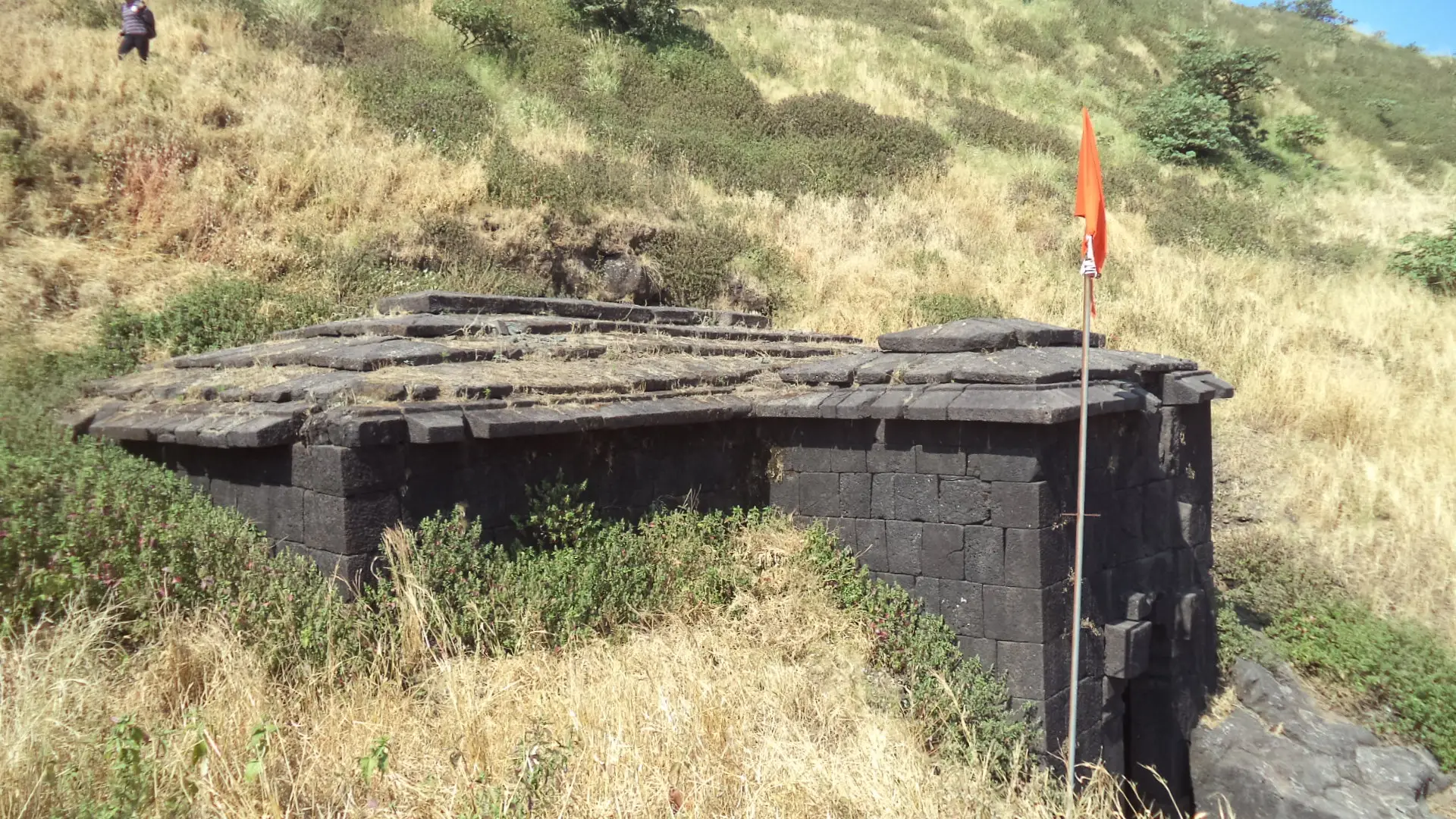 Stone-roofed rock-cut storehouse on the Jivdhan summit with a saffron flag beside it