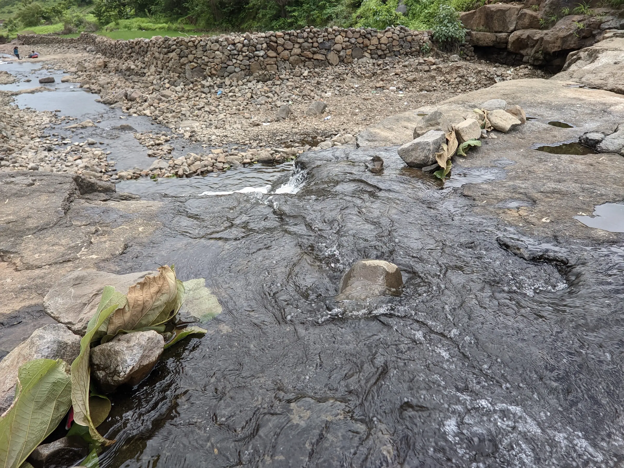 Shallow stream flowing over flat dark rock beside a stone check-wall on the path from Bhivpuri towards Sagachiwadi