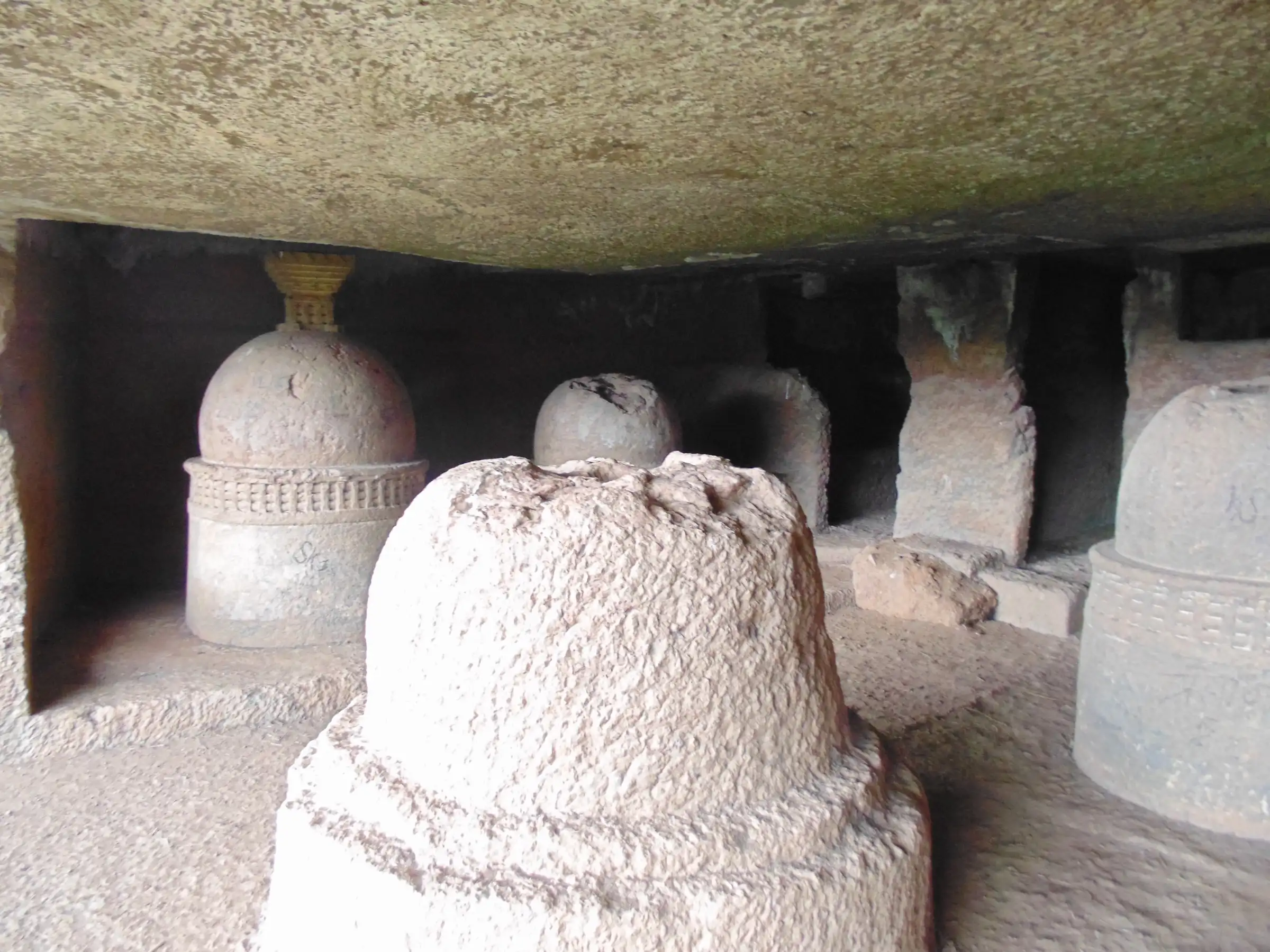Several rock-cut Buddhist stupas with railing patterns carved around their drums, inside a low hall at the Thanale caves