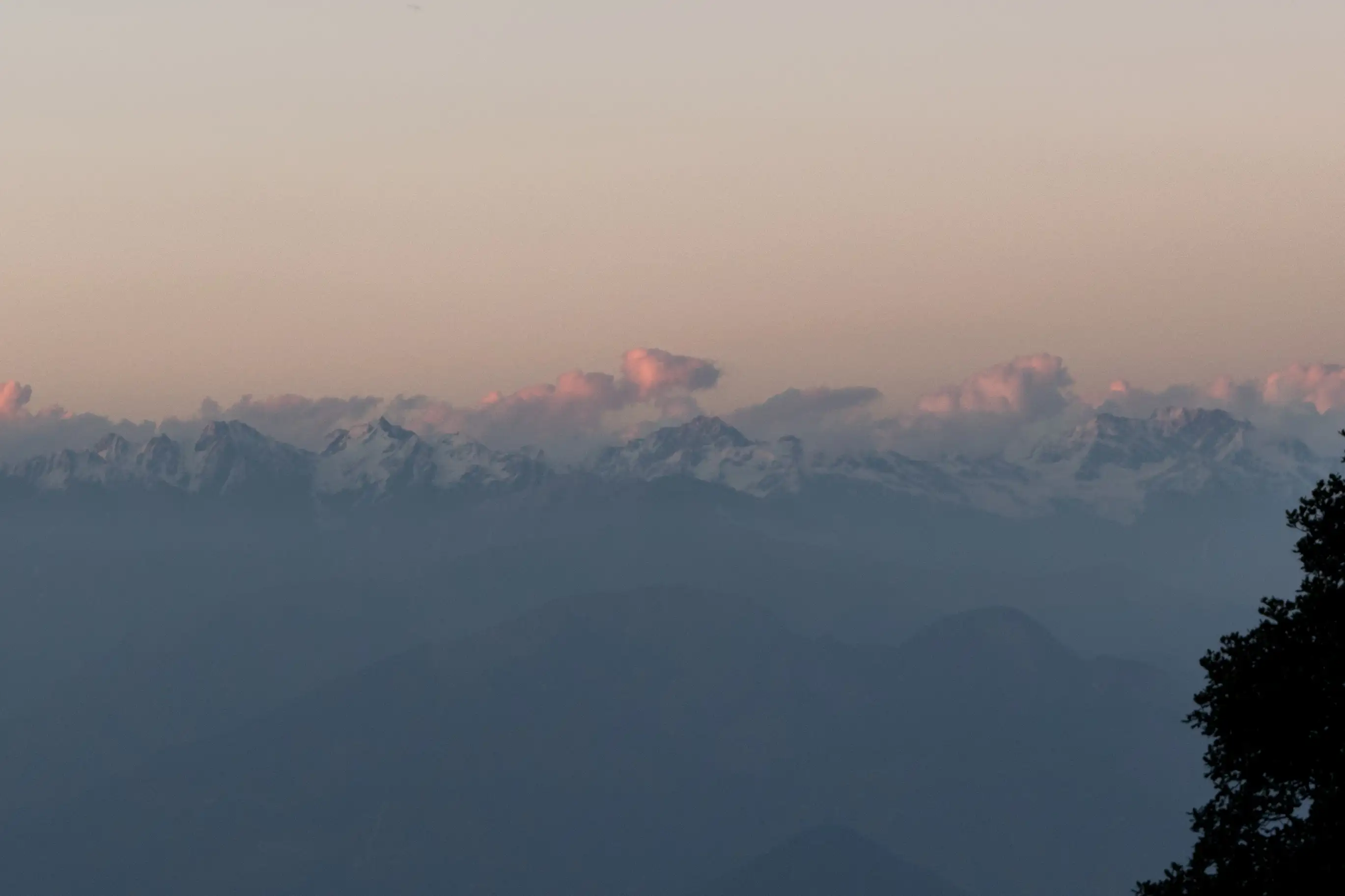 Snow peaks lit pink at dusk above hazy blue ridges, seen from Hatu Peak in the evening