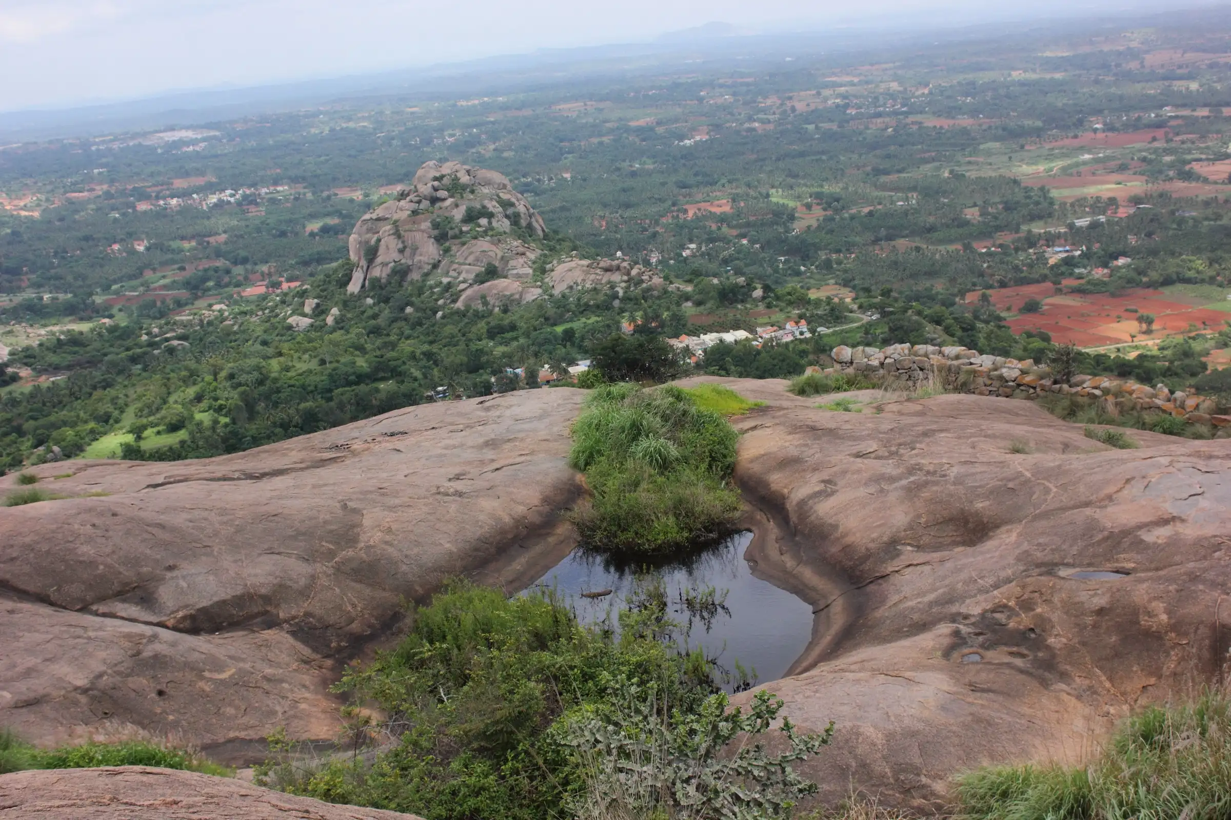 A small rock pool on the granite top of Hutridurga with farmland and distant hills below