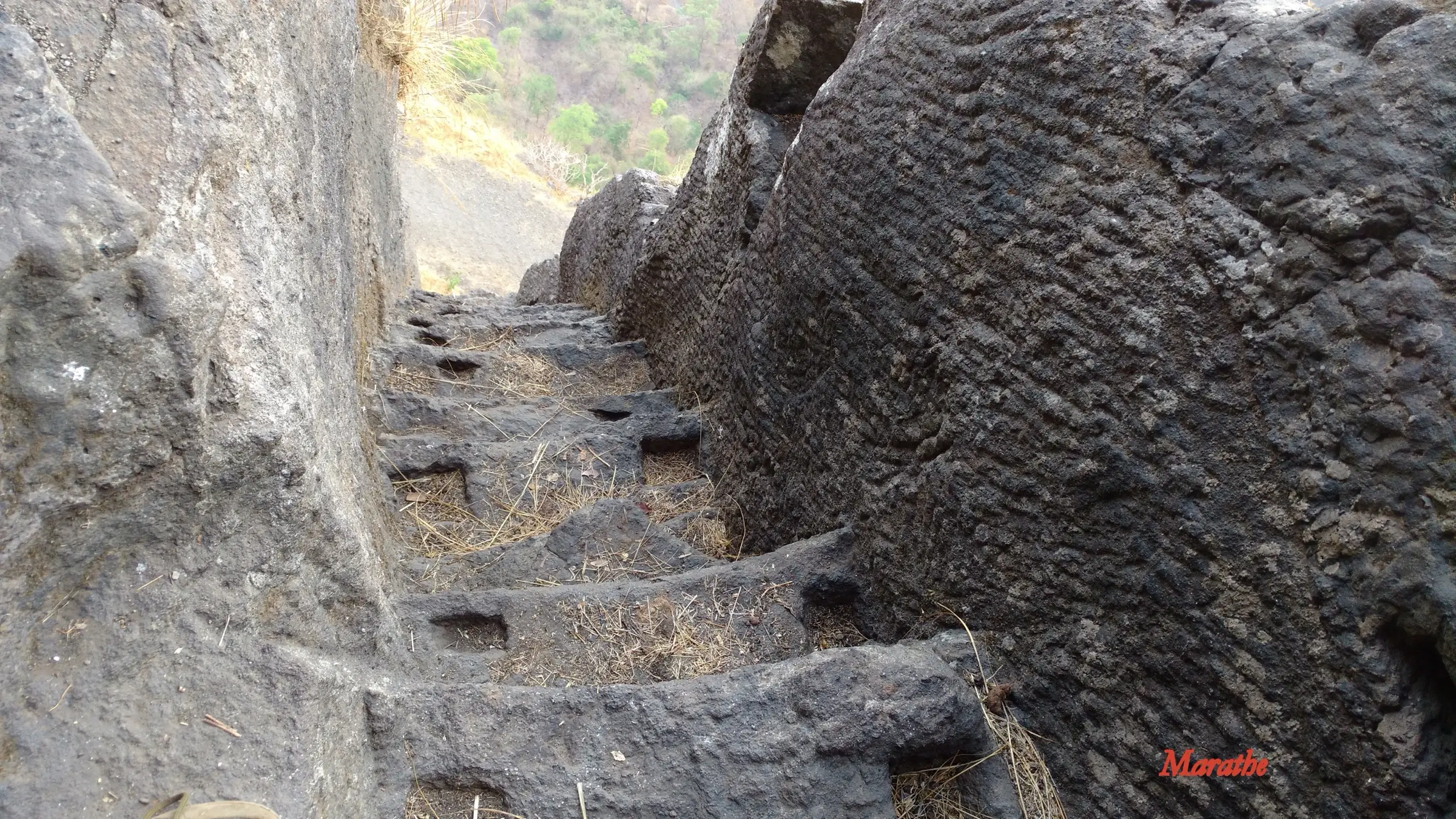 Narrow rock-cut steps with carved hand-holds climbing steeply between rock walls towards the top of Gorakhgad