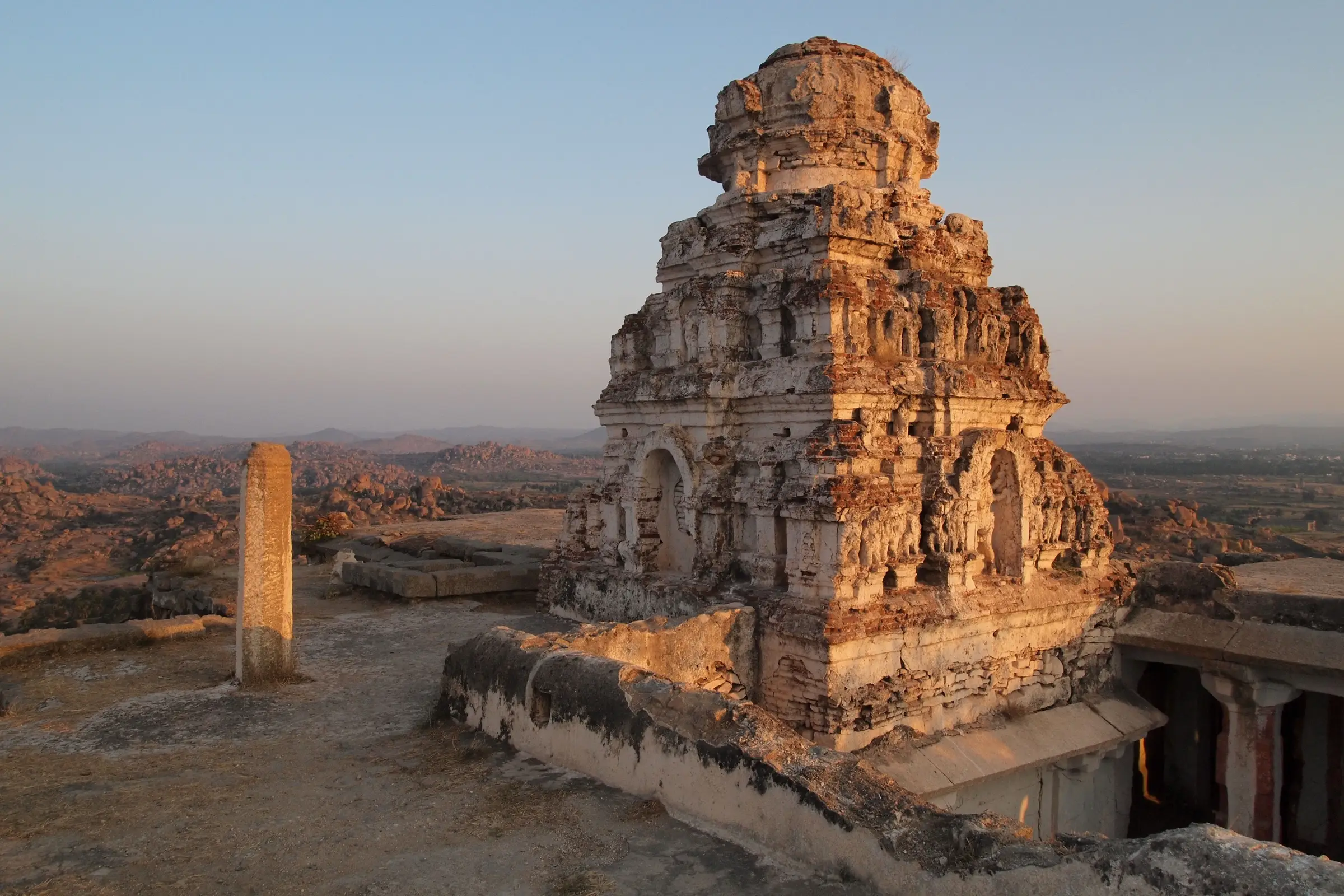 Stone tower of the Veerabhadra temple on the summit of Matanga Hill in evening light, with boulder hills behind
