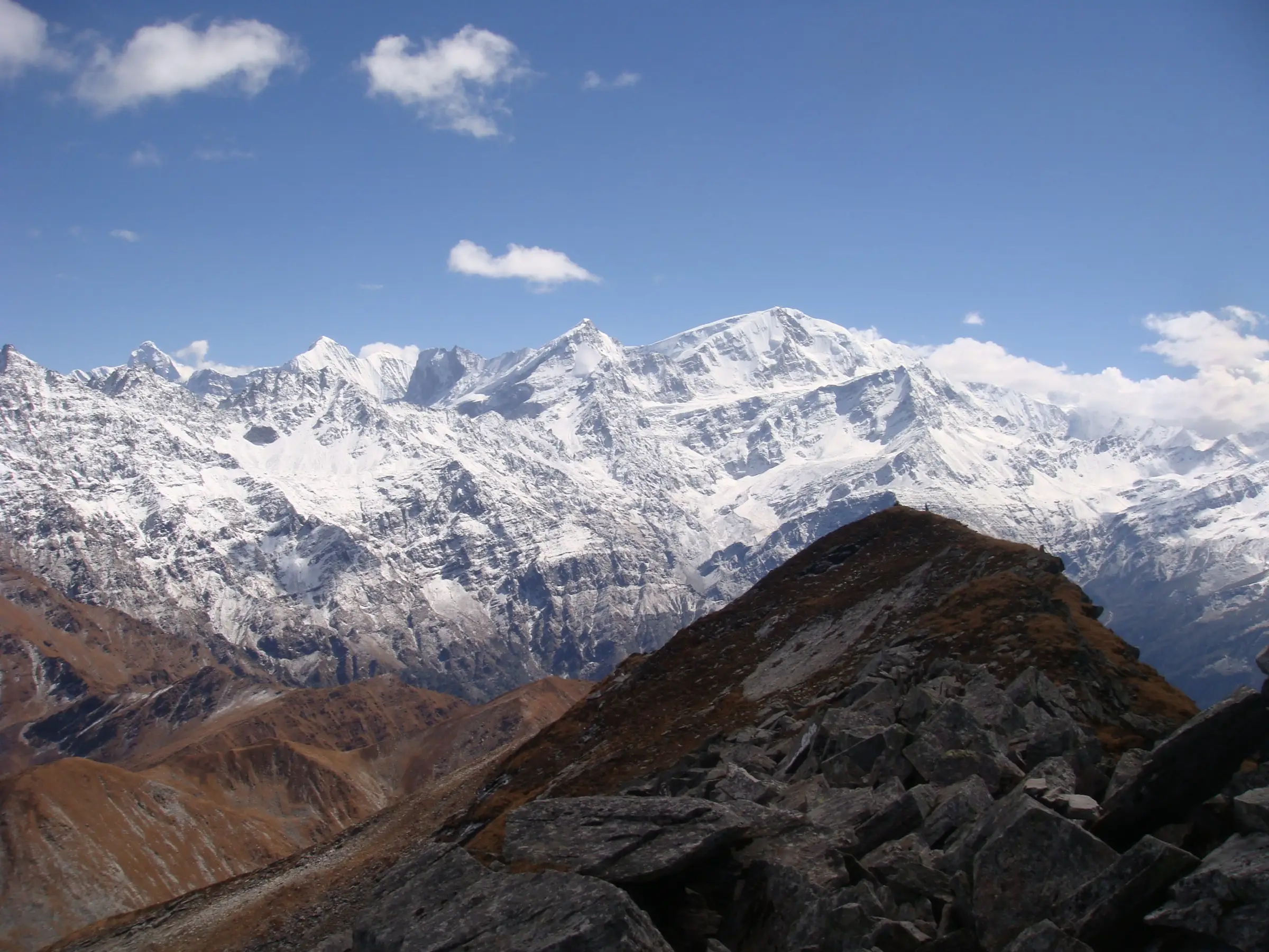 Snow-covered Garhwal Himalaya ridges seen from the rocky summit slopes of Pangarchulla under a blue sky