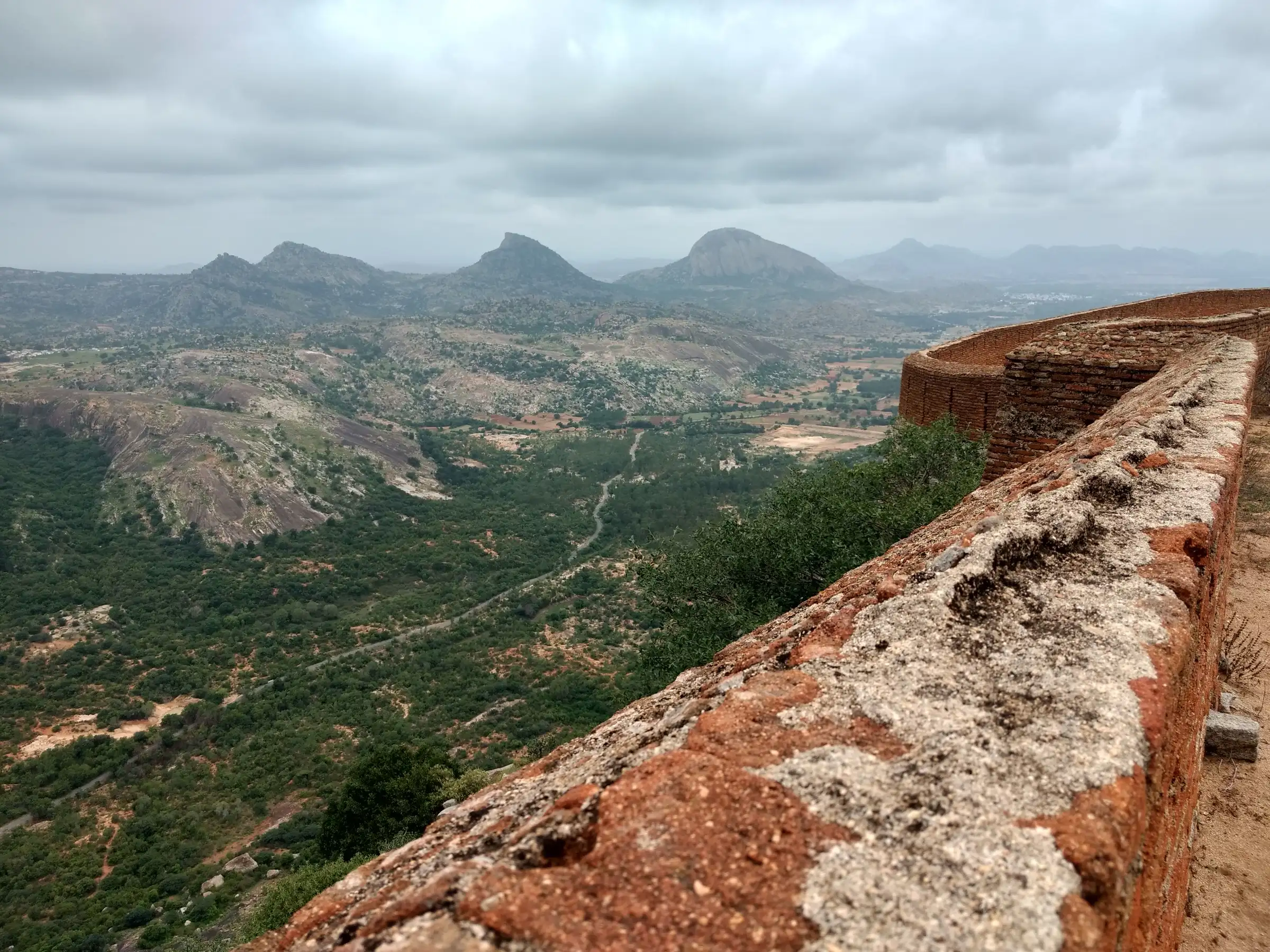 View from the fort wall at the top of Channarayana Durga over green scrub plains to rocky hills under cloud
