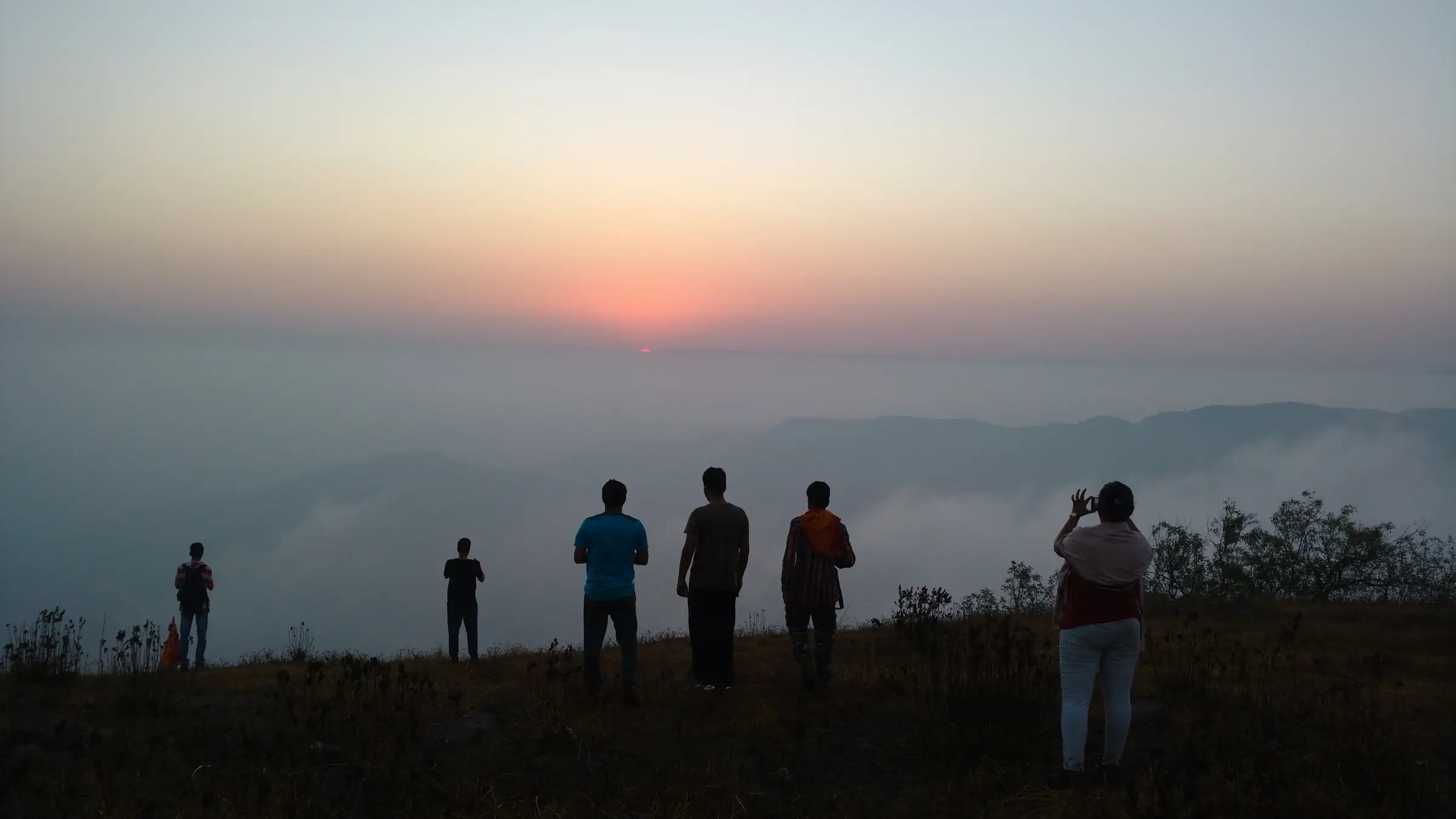 Trekkers silhouetted on the Manikgad fort top at sunrise, with cloud filling the valleys below