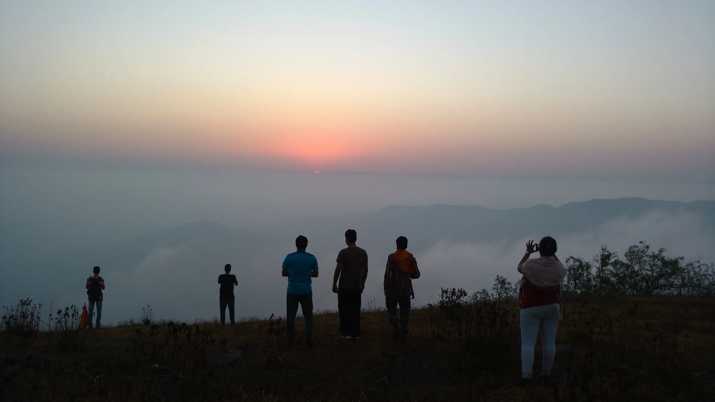 Trekkers silhouetted on the Manikgad fort top at sunrise, with cloud filling the valleys below