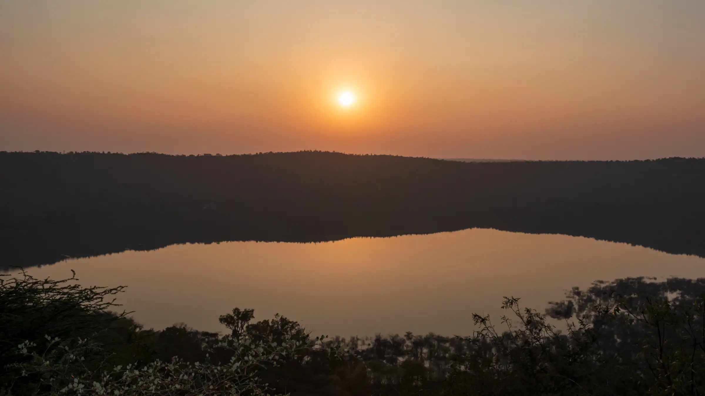 Sun setting over Lonar crater lake, the dark crater rim reflected in the still water