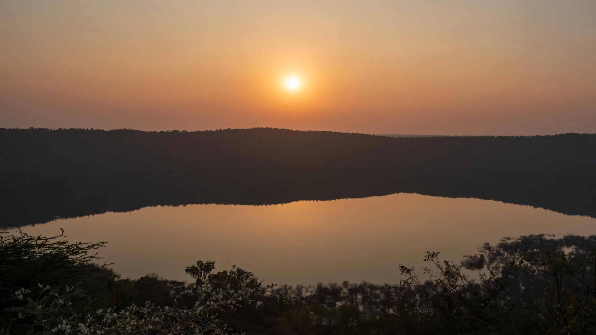 Sun setting over Lonar crater lake, the dark crater rim reflected in the still water