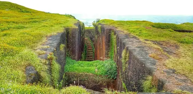 The sword-shaped rock-cut stepped well on Dategad, its steps leading down between laterite walls on a green plateau
