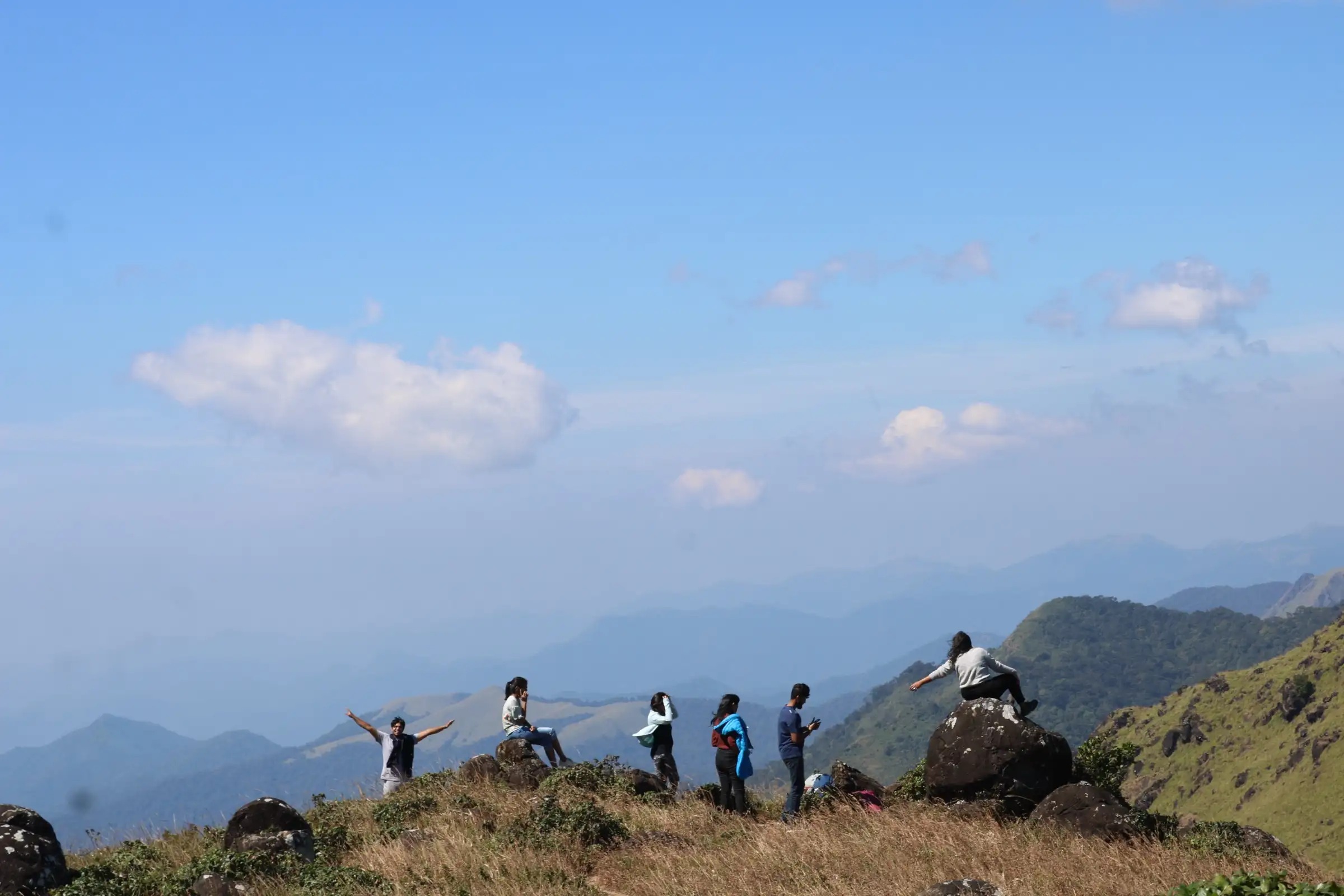 Trekkers on a grassy, boulder-strewn summit on Tadiandamol, the neighbouring peak visible from the Nelji ridge (not the Nelji trail itself)