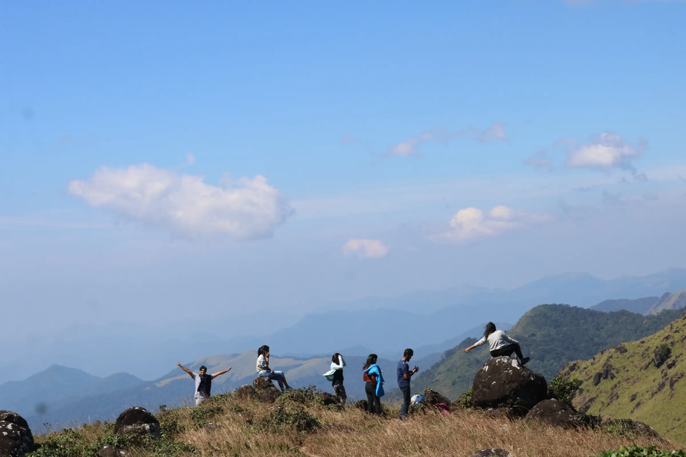 Trekkers on a grassy, boulder-strewn summit on Tadiandamol, the neighbouring peak visible from the Nelji ridge (not the Nelji trail itself)