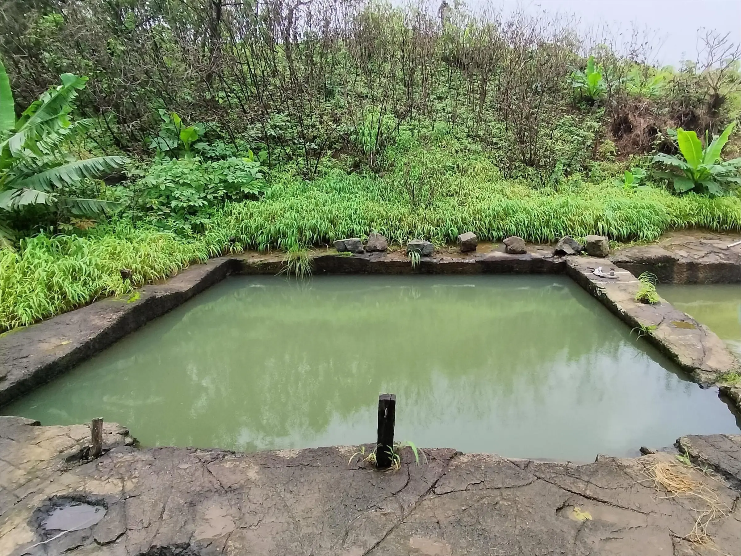 A square rock-cut water cistern filled with green water on top of Takmak Fort
