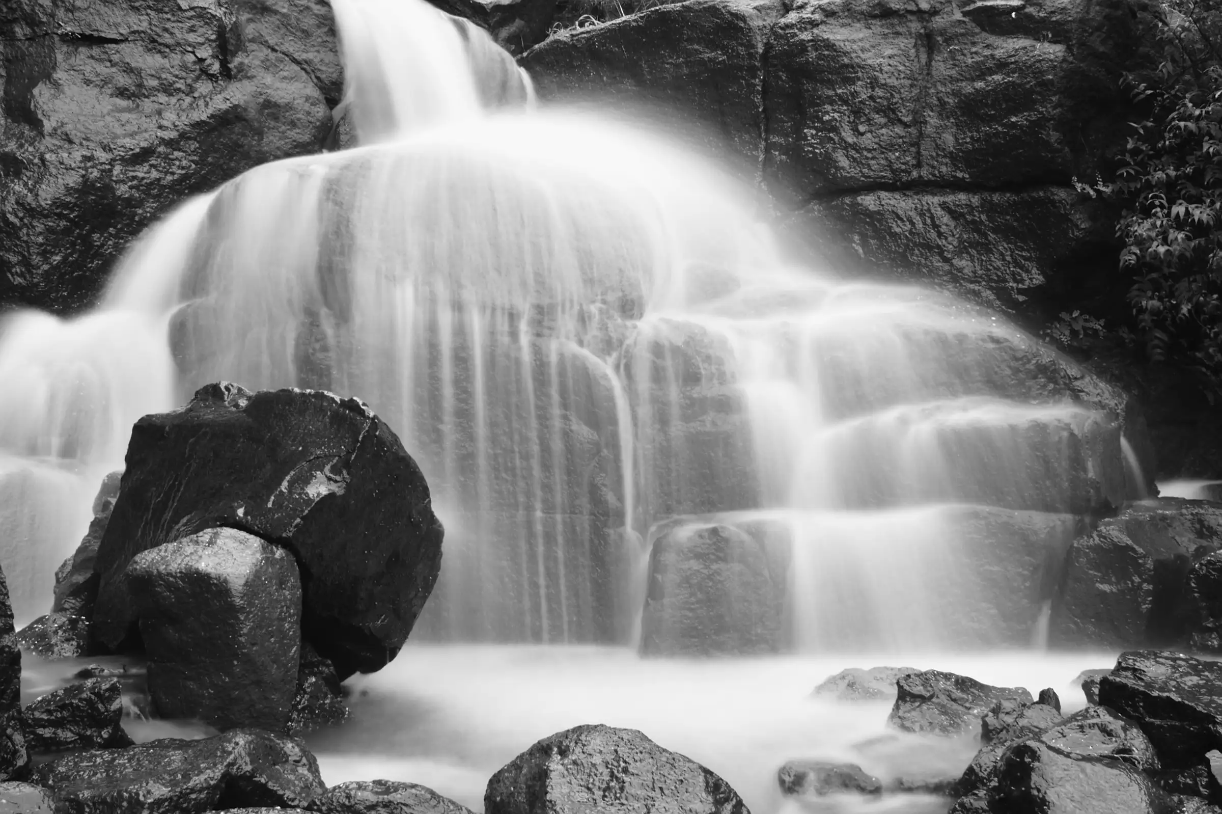 Black-and-white long exposure of a monsoon waterfall spilling over stepped rock in Tamhini Ghat, near the trek (not Milkybar Waterfall itself)