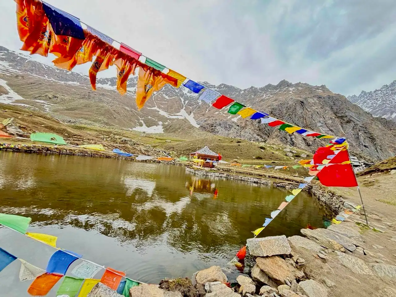 Prayer flags strung across the Yulla Kanda lake with the Krishna temple in the distance and snow patches on the mountains