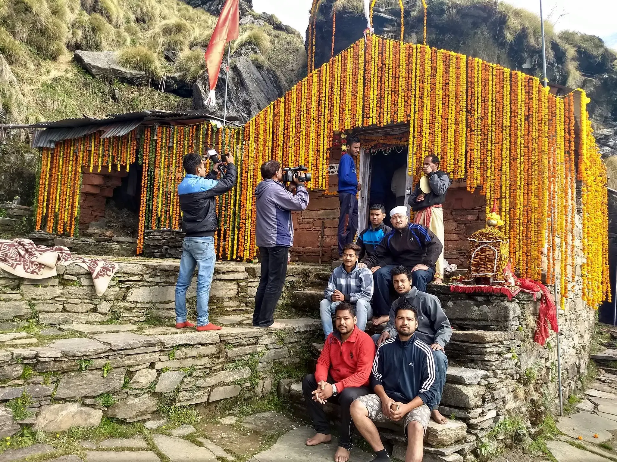 Rudranath temple decorated with garlands of marigold, with pilgrims seated on the stone steps in front